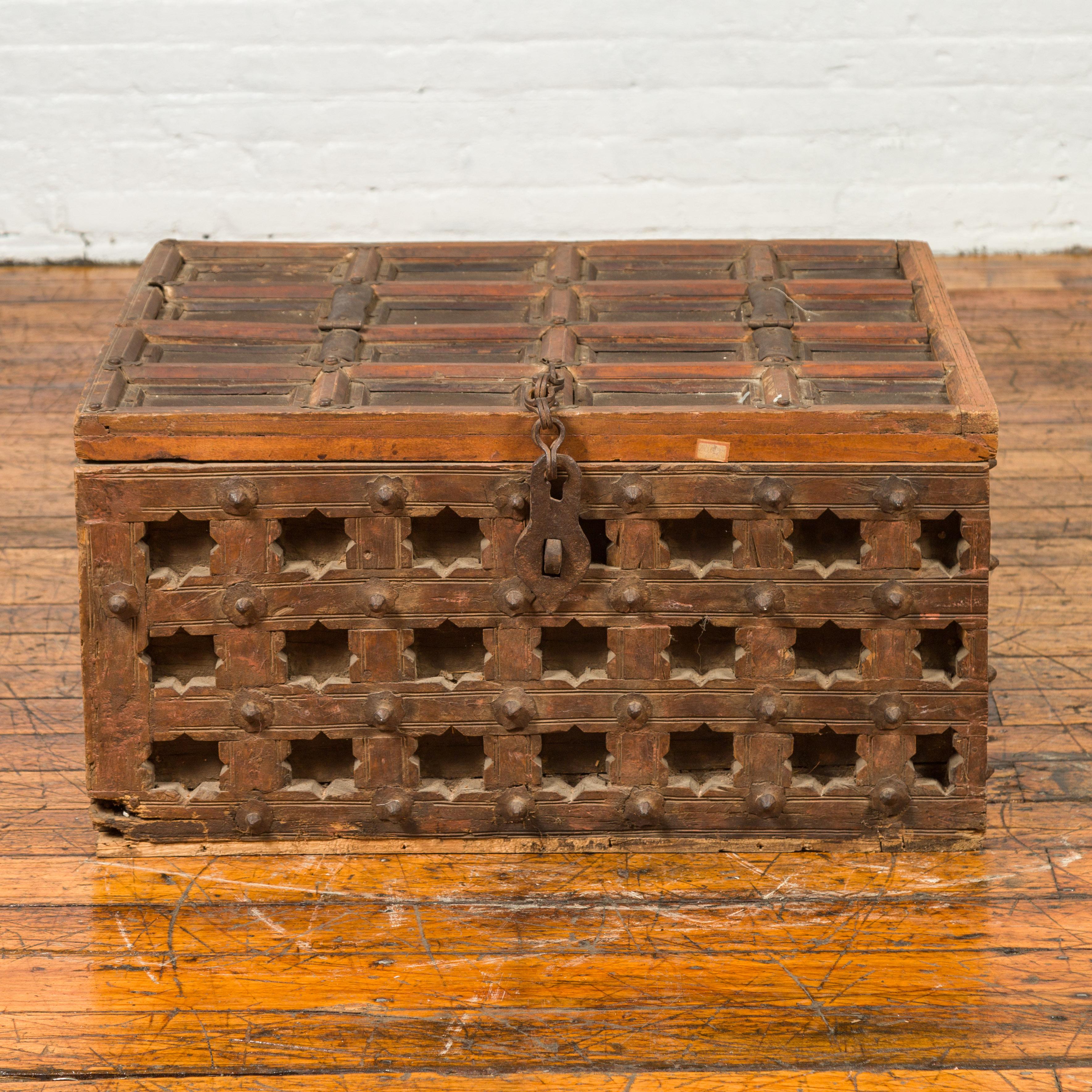 An antique Indian wooden treasure chest from the 19th century, with paneled top, pierced stars and iron hardware. Found in a courtyard, this wooden treasure chest charms us with its weathered appearance and pierced motifs. The rectangular paneled