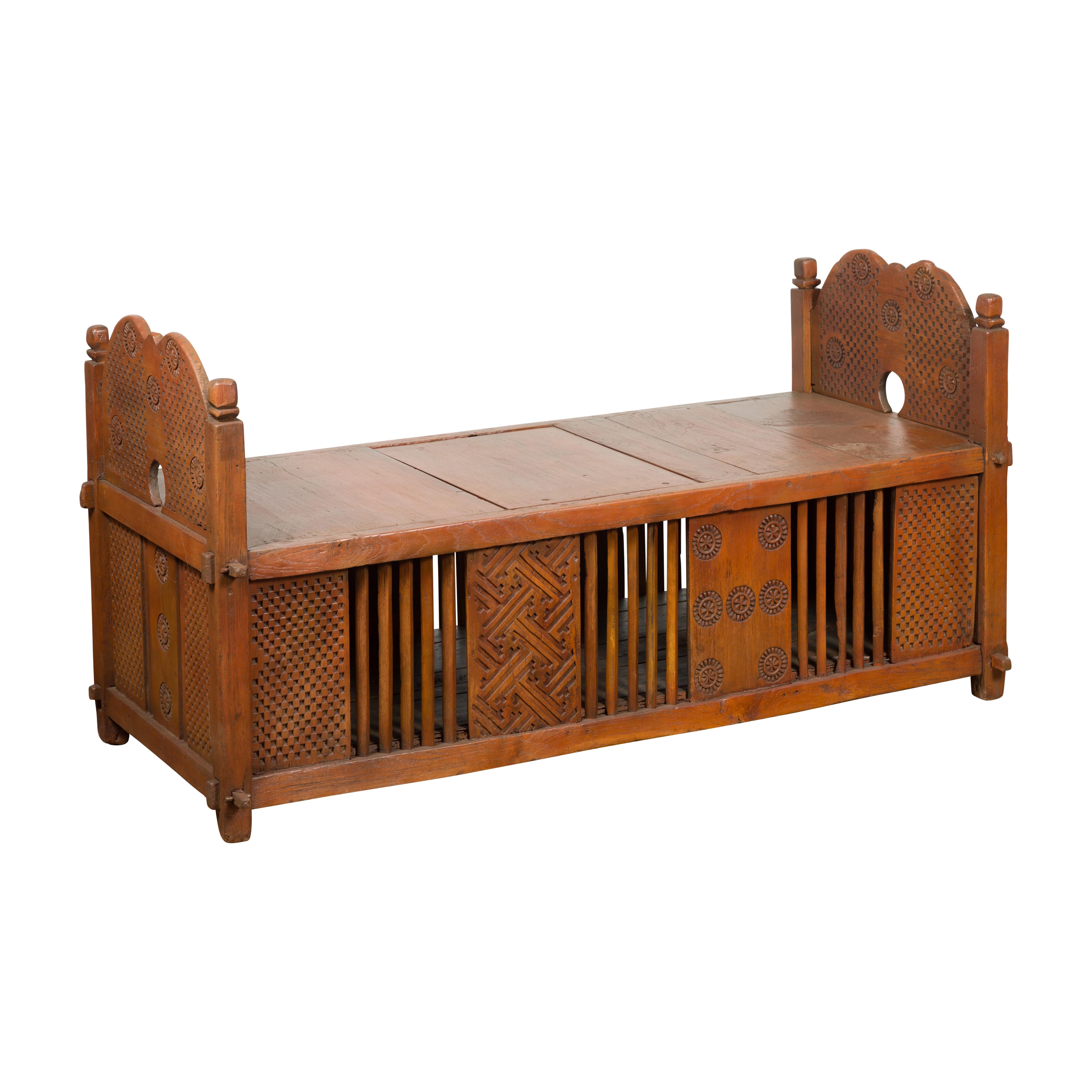 An antique Indian window bench from the 19th century with internal storage space and carved geometric motifs alternating with slatted panels. Discover the captivating beauty of this antique Indian window bench from the 19th century. Crafted with