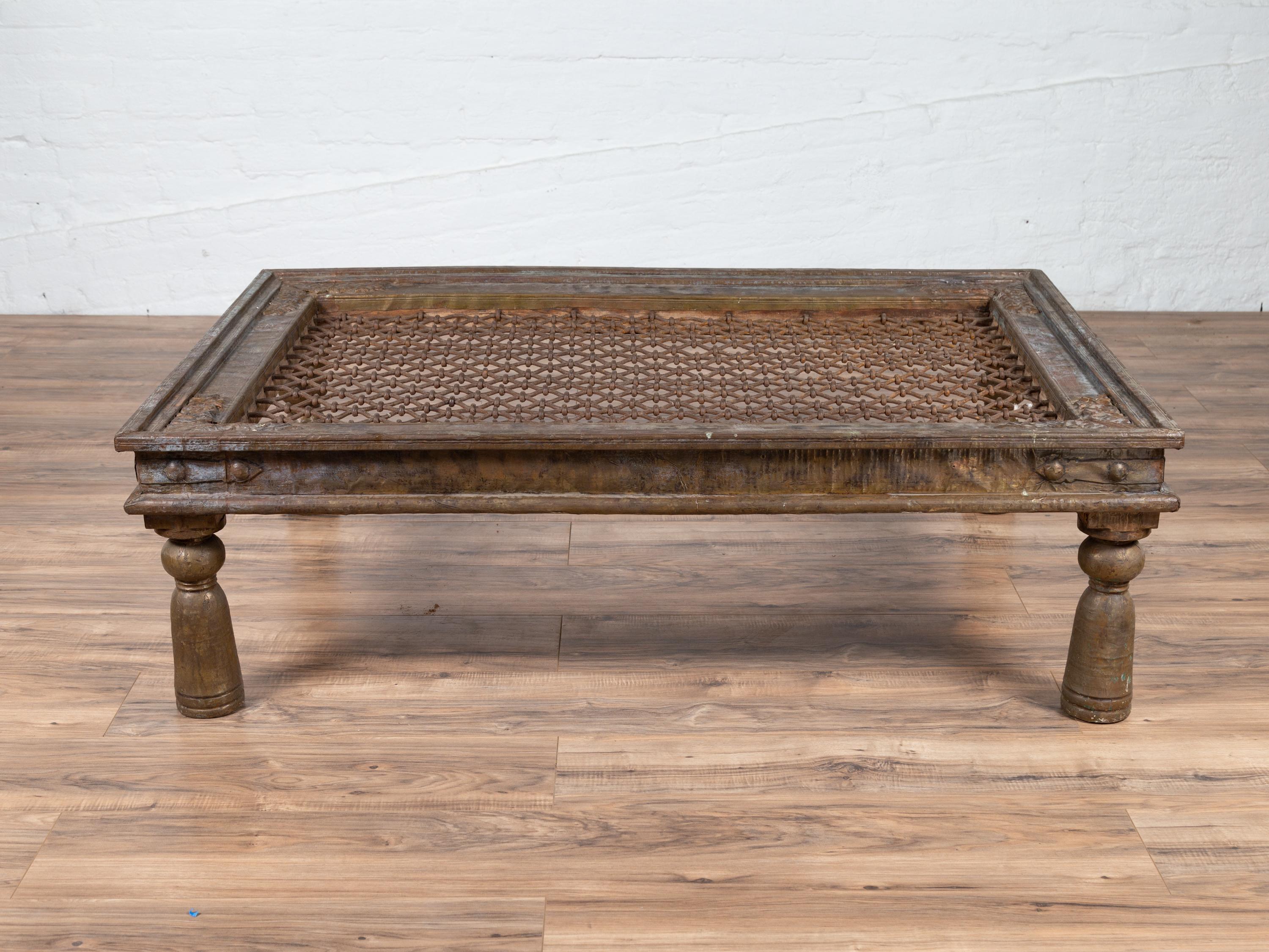 An Indian coffee table made of an antique window grate inset into a wooden structure accented with metal sheathing. Born in India during the early years of the 20th century, this Indian window grate is resting on four turned baluster-type legs and