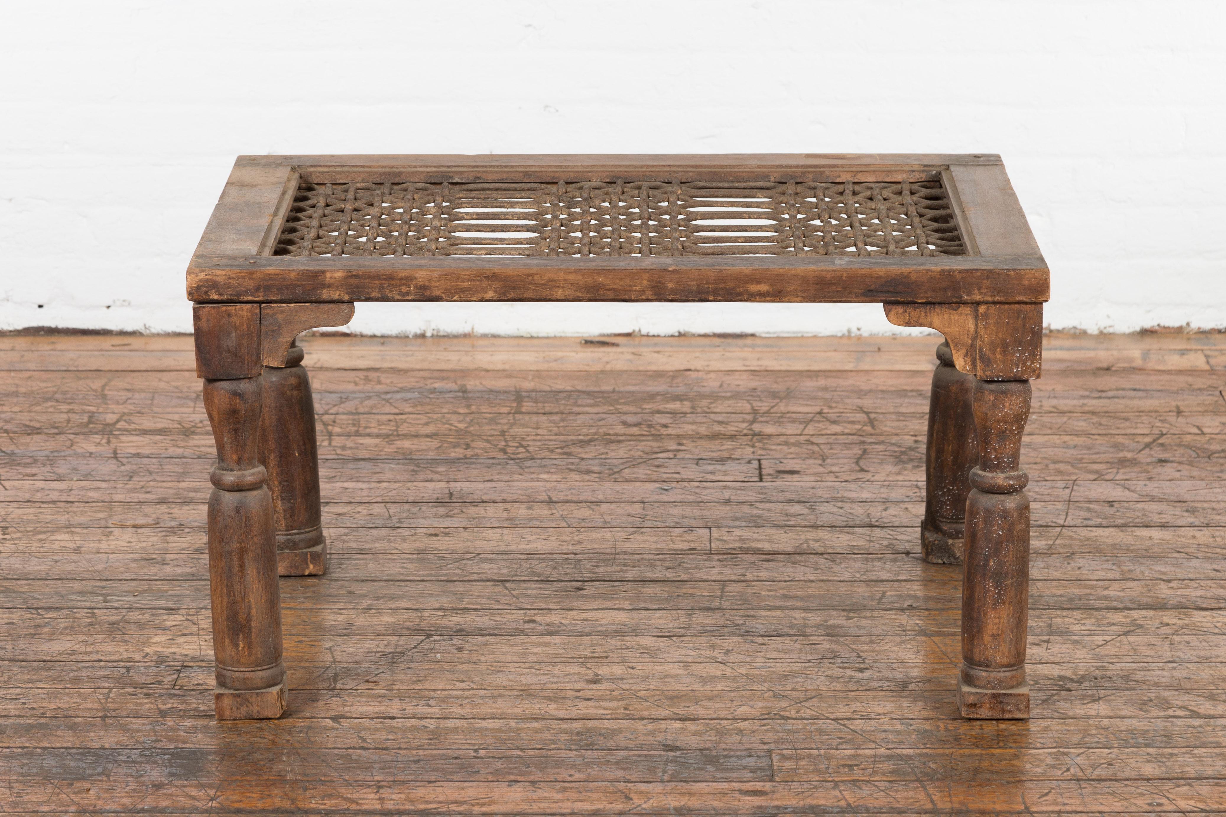 An antique rustic Indian window grate from the 19th century, made into a coffee table with baluster legs and weathered appearance. We have more assorted sizes available, please contact us with any questions. Created in India during the 19th century,