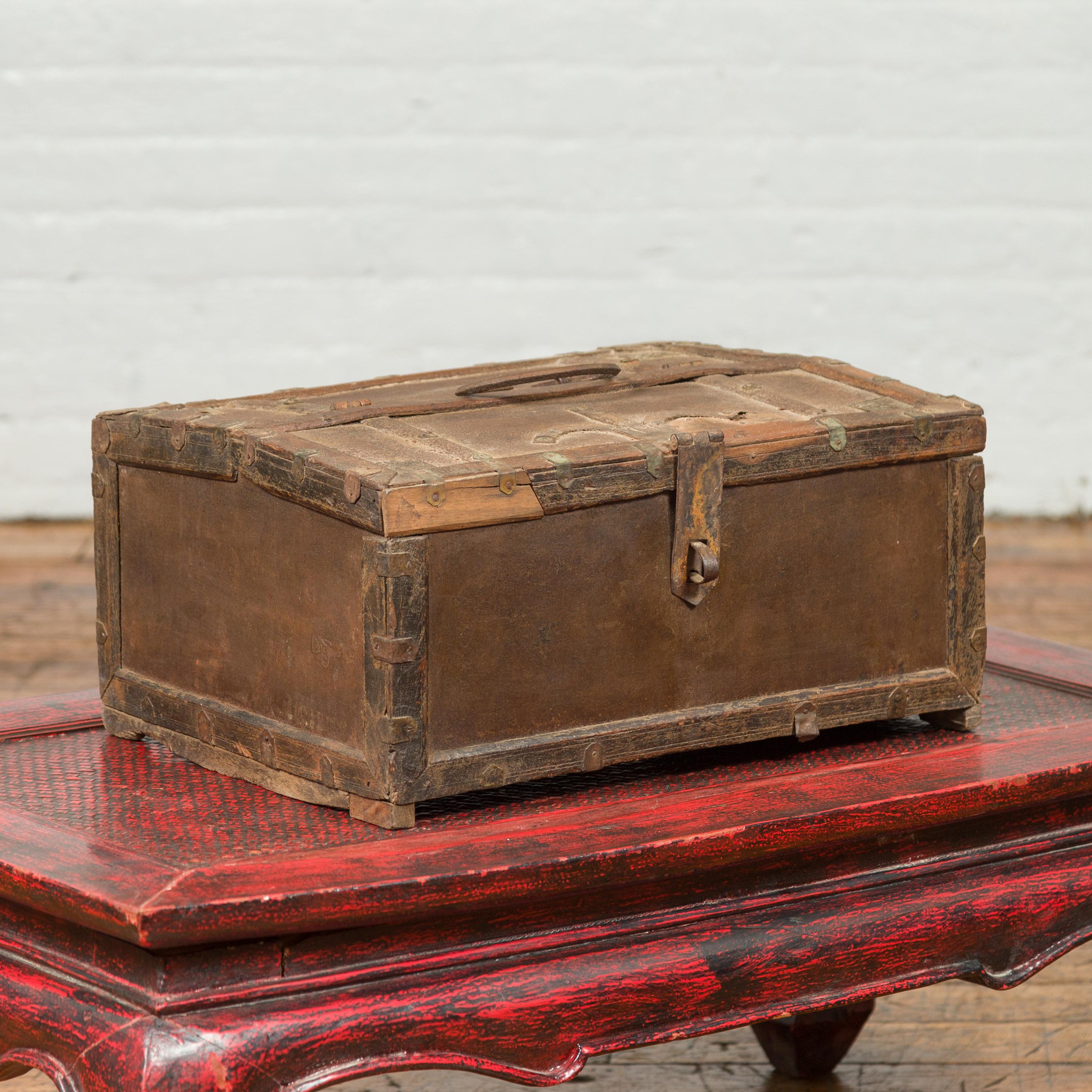 An antique Indian wooden box from the 19th century with iron hardware and weathered appearance. Topped with a rectangular lid half opening to reveal a partitioned interior, this old cash box is raised on petite feet. Boasting a charming air of