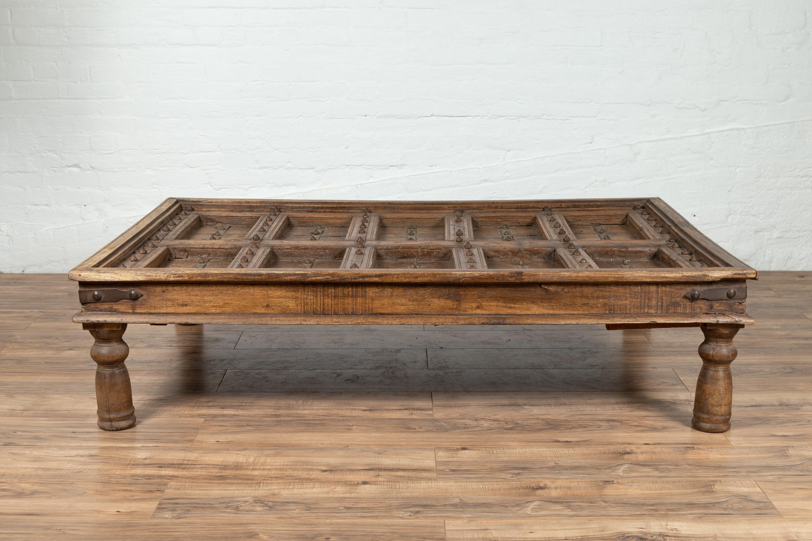 An antique Indian palace wooden door made into a coffee table with iron accents and baluster legs. Born in India during the early years of the 20th century, this exquisite palace door has been made into a coffee table. The top is rhythmically