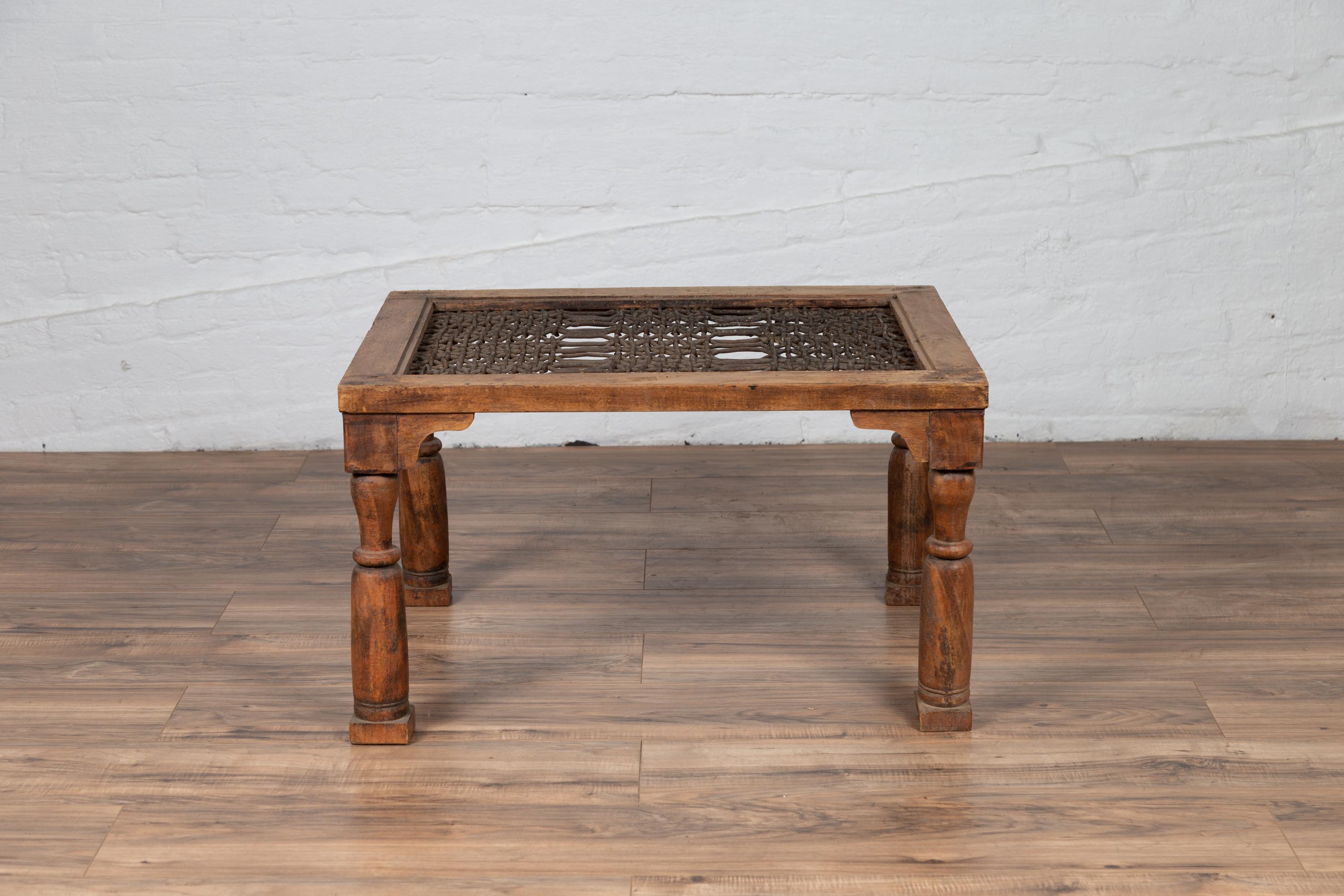An antique Indian side table from the 19th century with window grate top, turned legs and spandrels. Born in India during the 19th century, this Indian coffee table features a rectangular top made of an iron window grate, resting on four turned