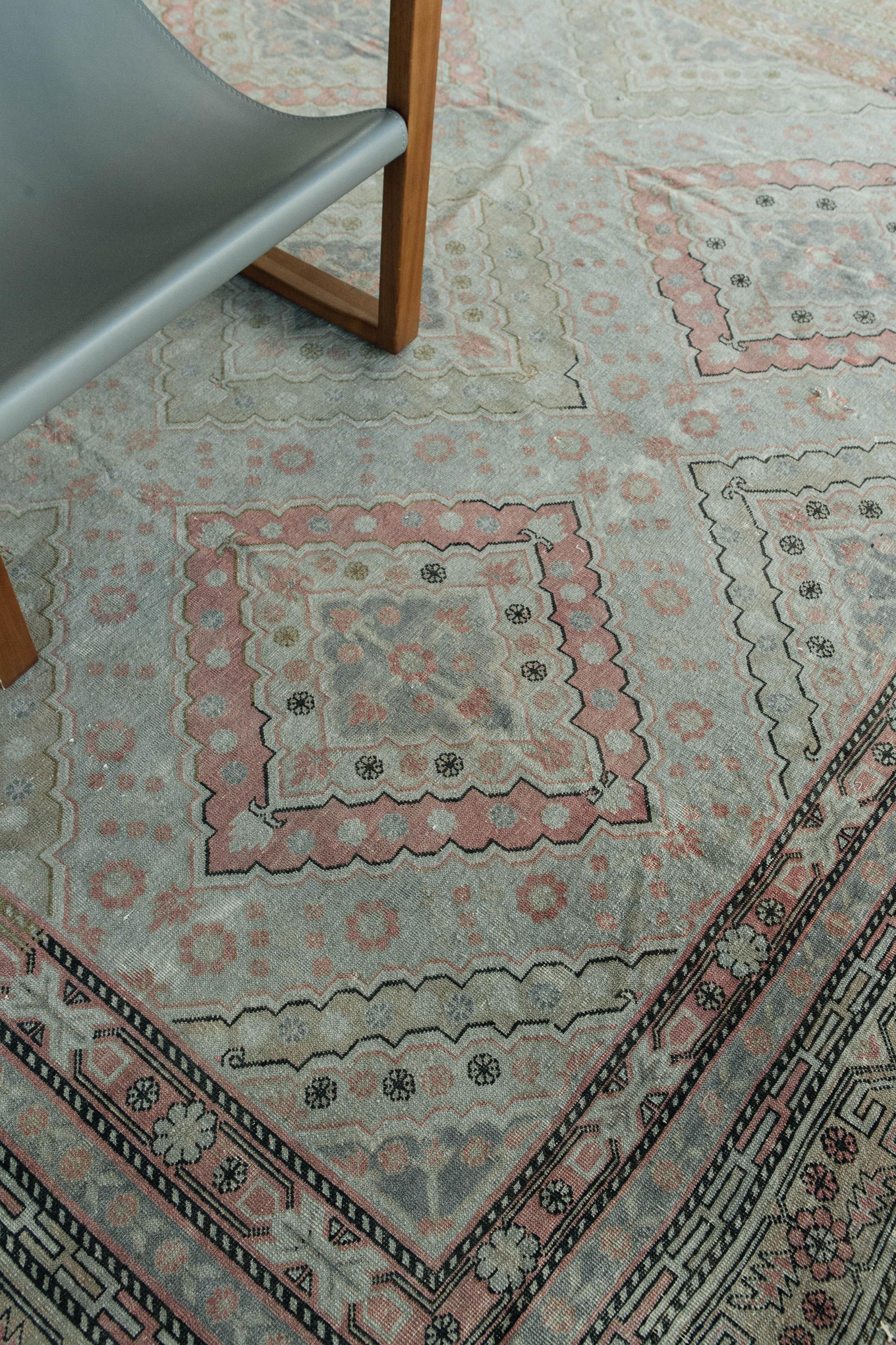 Antique rug of Indo-Pakistani origin in a muted palette of blue-grey, sage green, rose and sand with irregularly distressed dark outline. Decorative all-over motif of diamond pattern with concentric internal shapes. Geometric and stylized floral