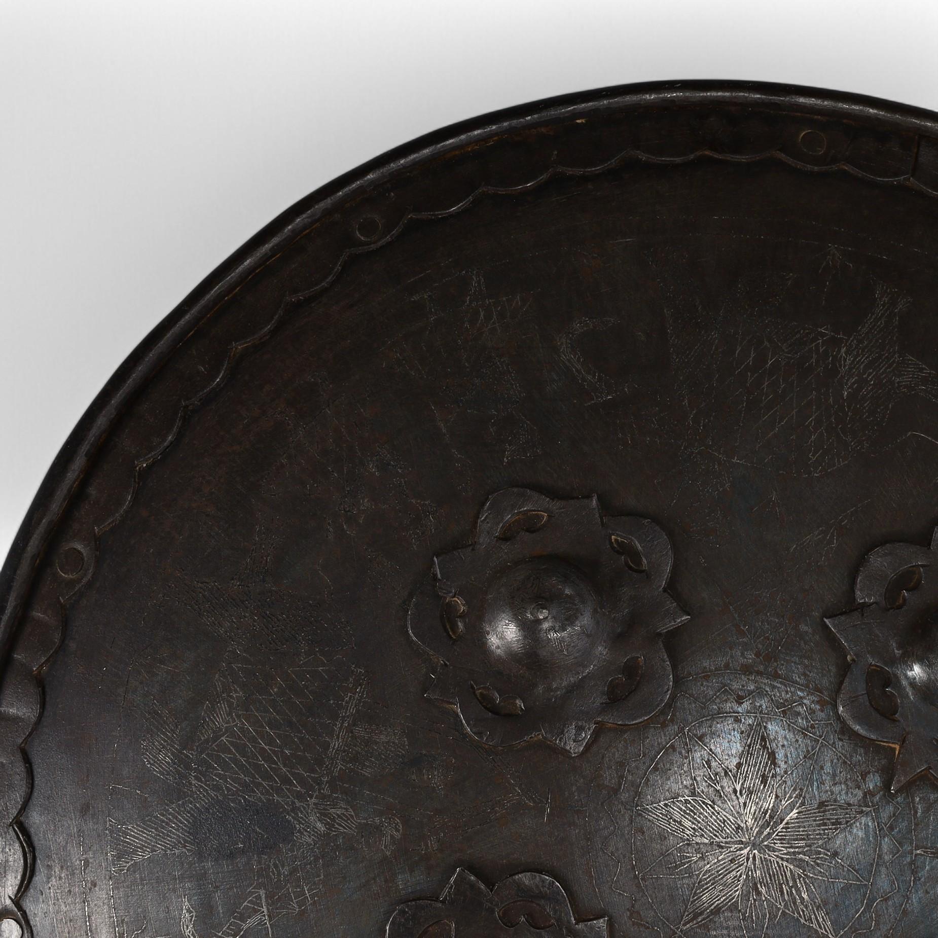 Intrigante scudo storico indo-persiano del XIX secolo realizzato a mano in acciaio e decorato con quattro protuberanze floreali e figure incise, che conserva i manici originali in pelle. 