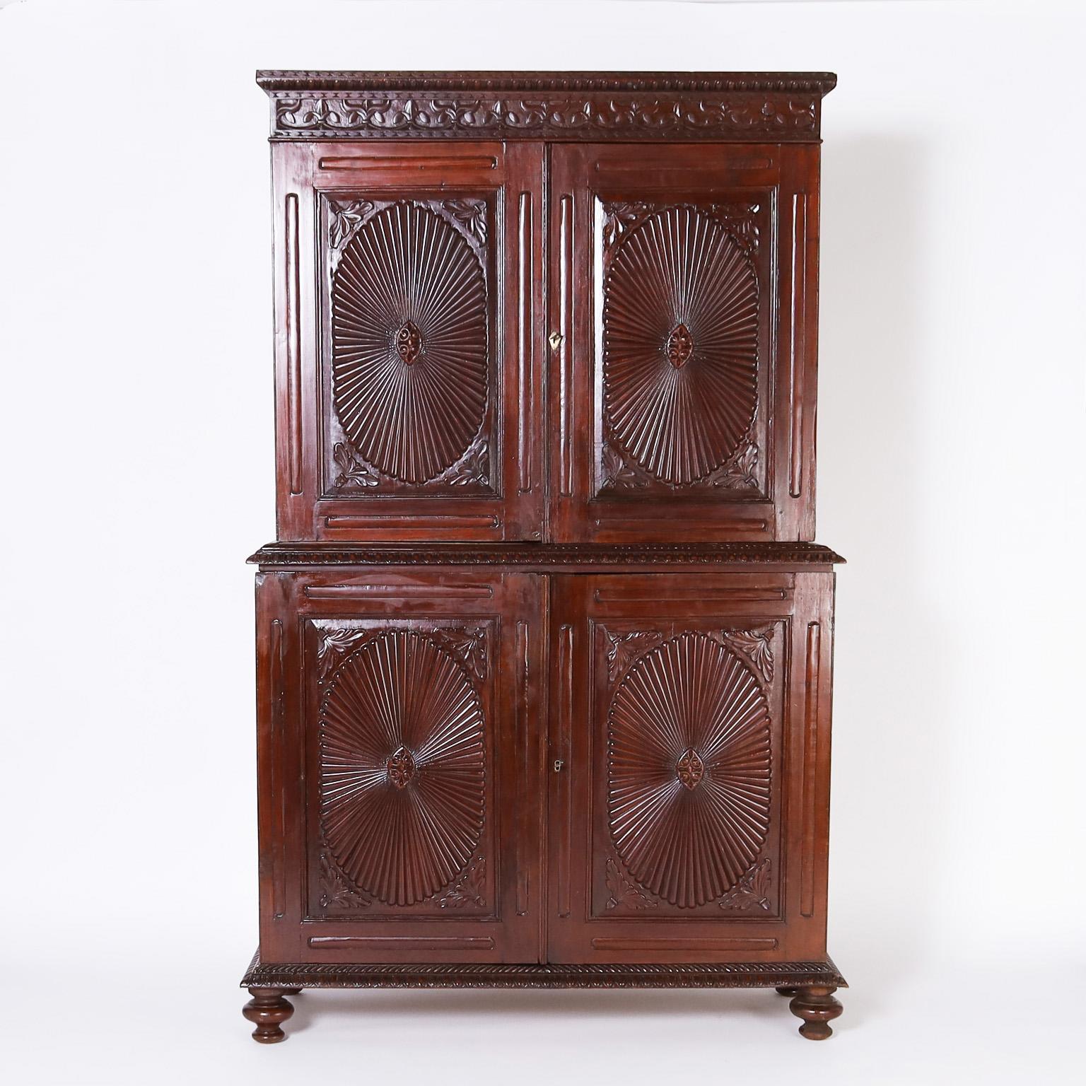 Rare and remarkable 19th century Indo Portuguese four door cabinet featuring an egg and dart top cornice over a floral carved band, four carved sunbursts on the front, plenty of storage inside, working keys and turned feet under a lower carved