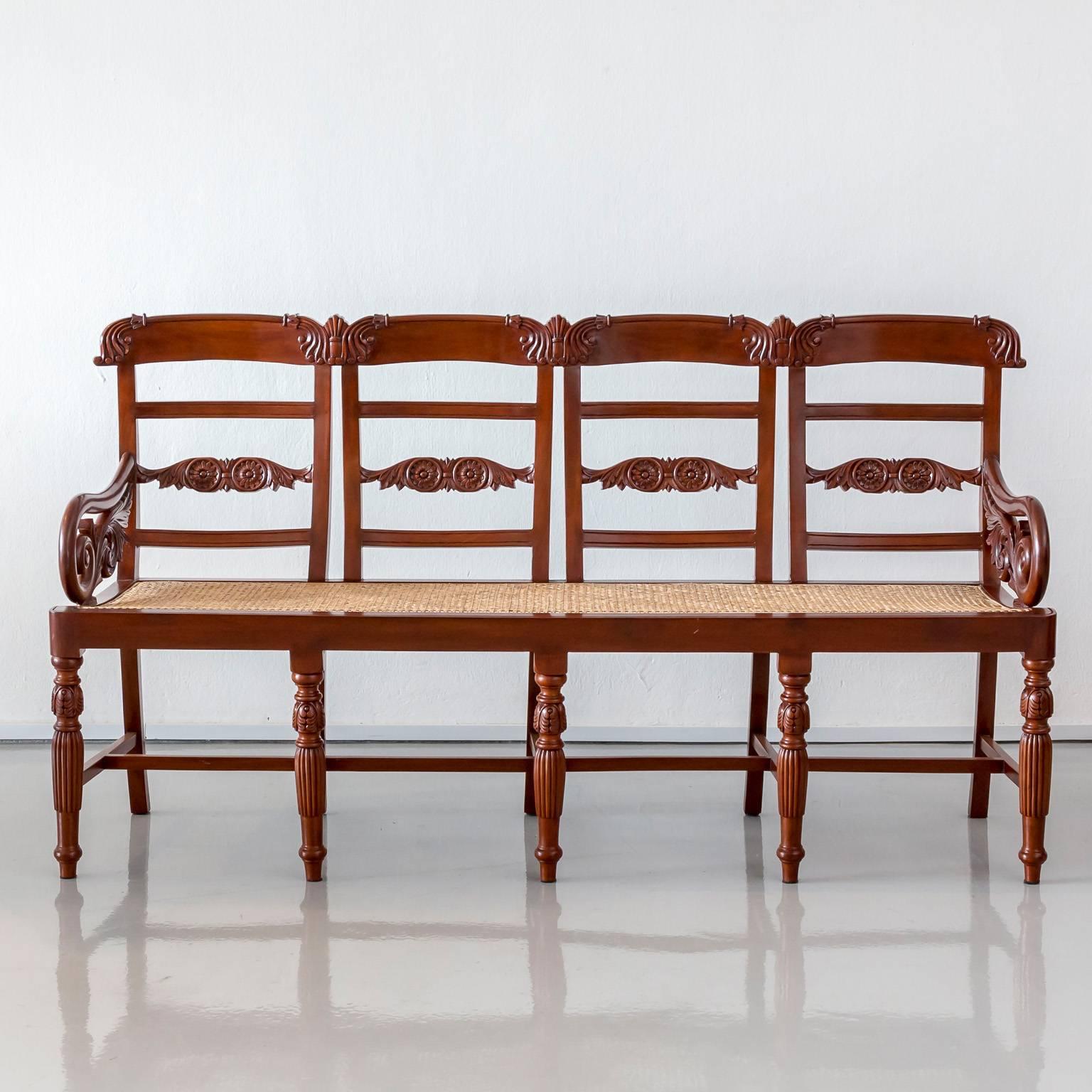 A beautifully carved Portuguese colonial mahogany settee with a quadruple back and newly caned seat. The shaped individual chair backs and rolled armrests are carved with a floral pattern. The settee stands on five reeded and tapered front legs and