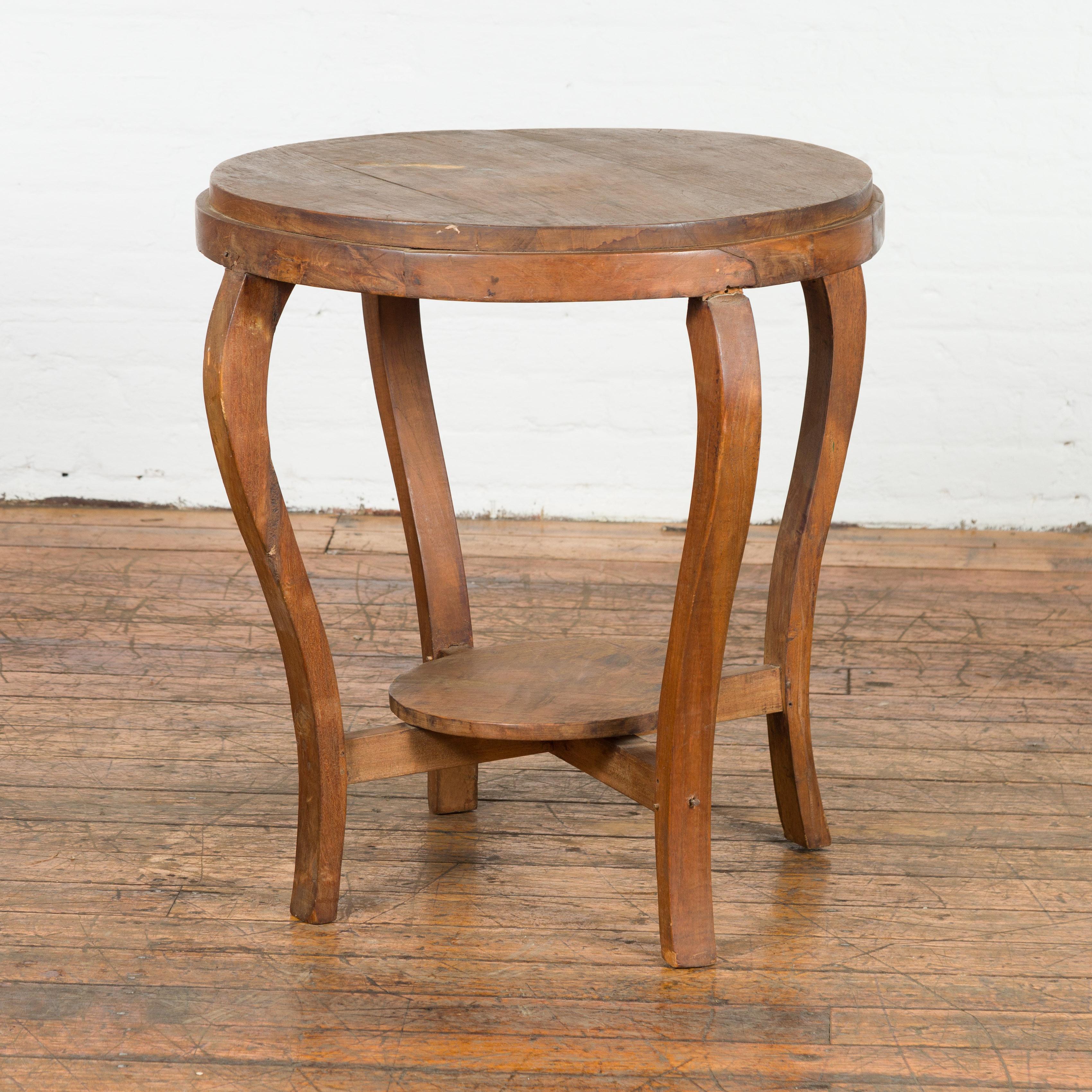1900s Antique End Table with Curved Legs & Lower Shelf Embodying early 20th-century Indonesian craftsmanship. This  side table carries an air of whimsical elegance. The table effortlessly melds functionality with a simple aesthetic, ensuring it
