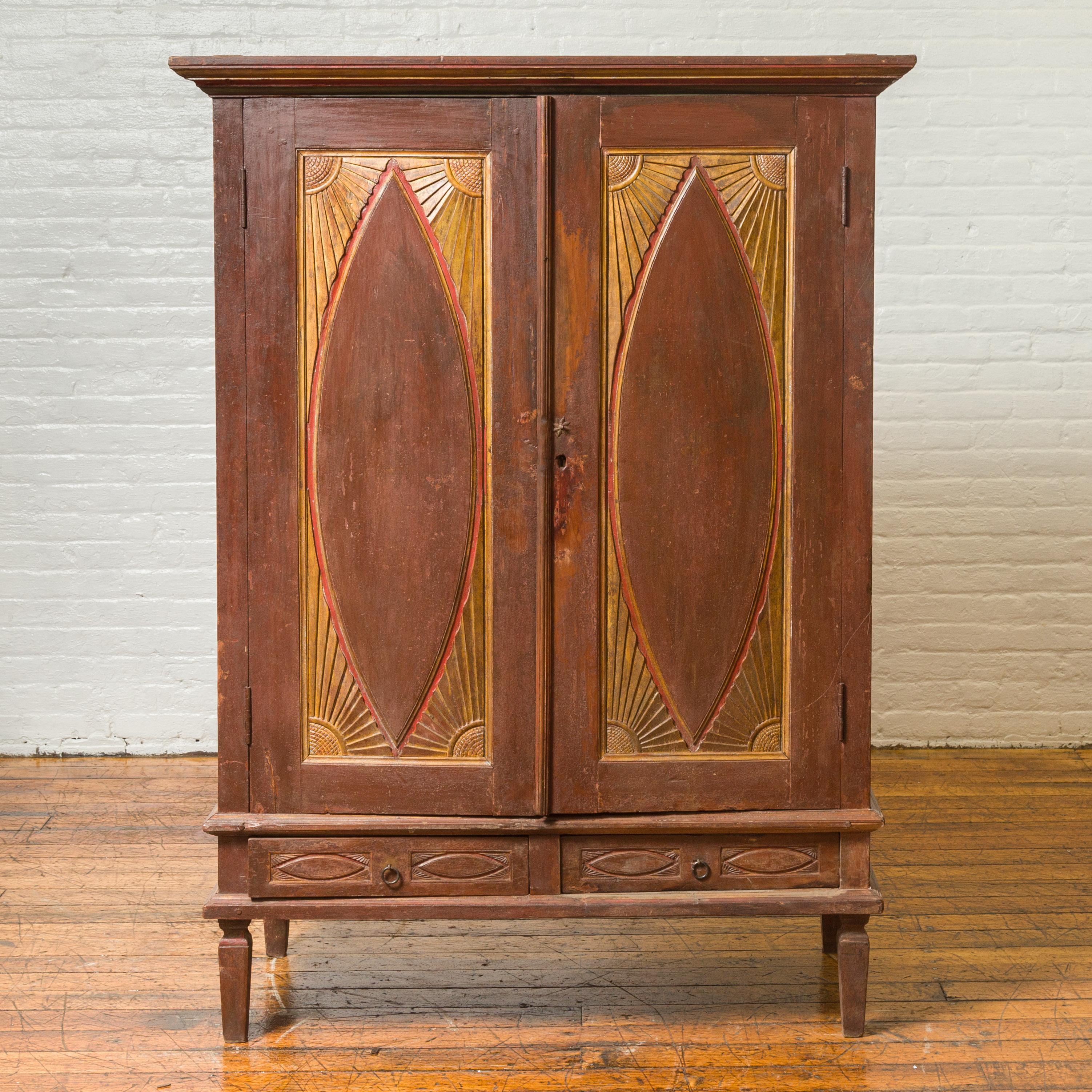 An antique Indonesian wooden cabinet from the 19th century, with carved doors and radiating motifs. Crafted in Indonesia, this wooden cabinet attracts our attention with it elongated almond-style motifs, surrounded by sun rays in the corners and its