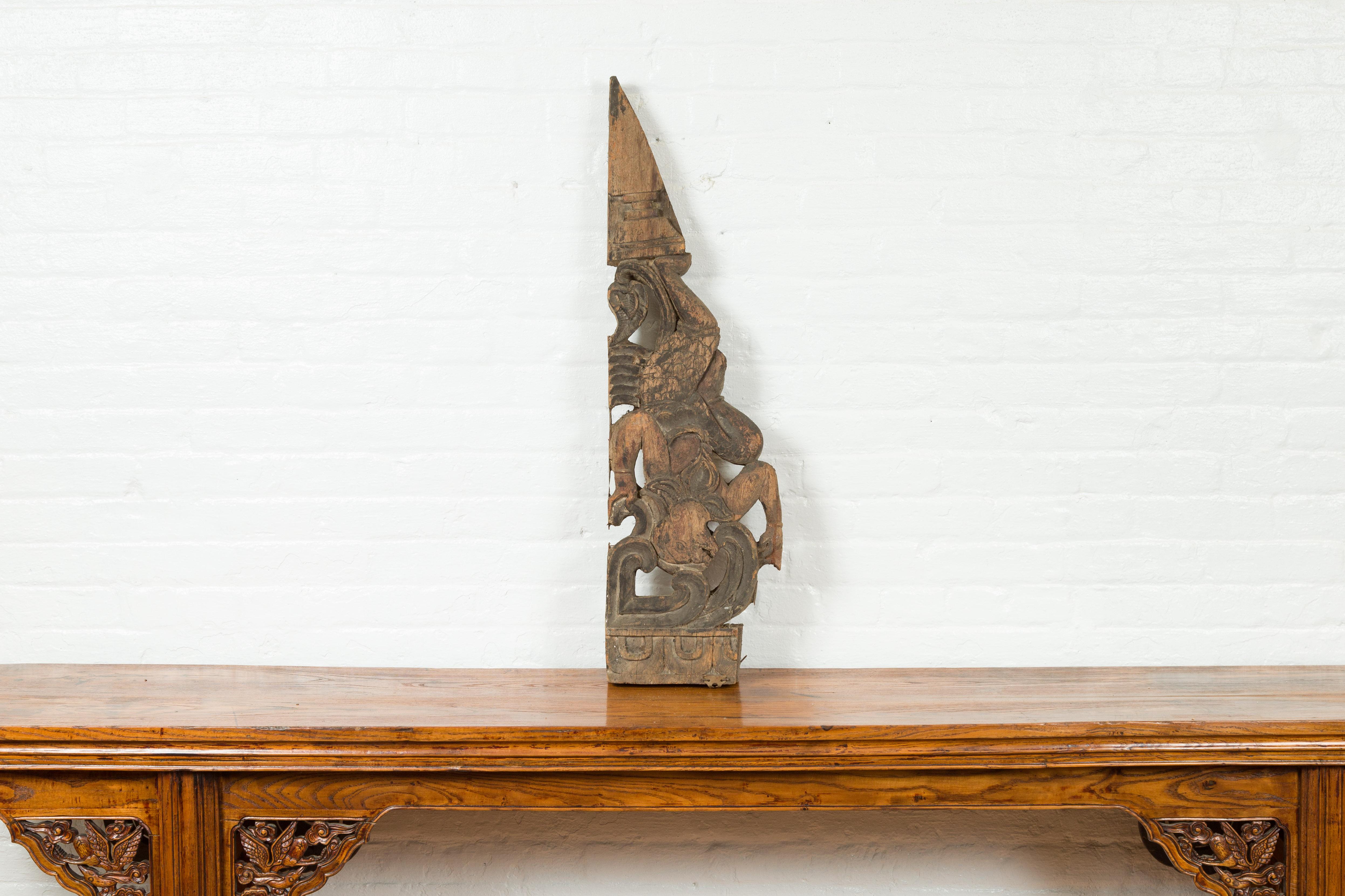 An antique Indonesian carved wooden triangular architectural fragment from the 19th century, with falling figure. Hand carved in Indonesia, this architectural fragment features a triangular shape and a nicely distressed patina. A falling figure,