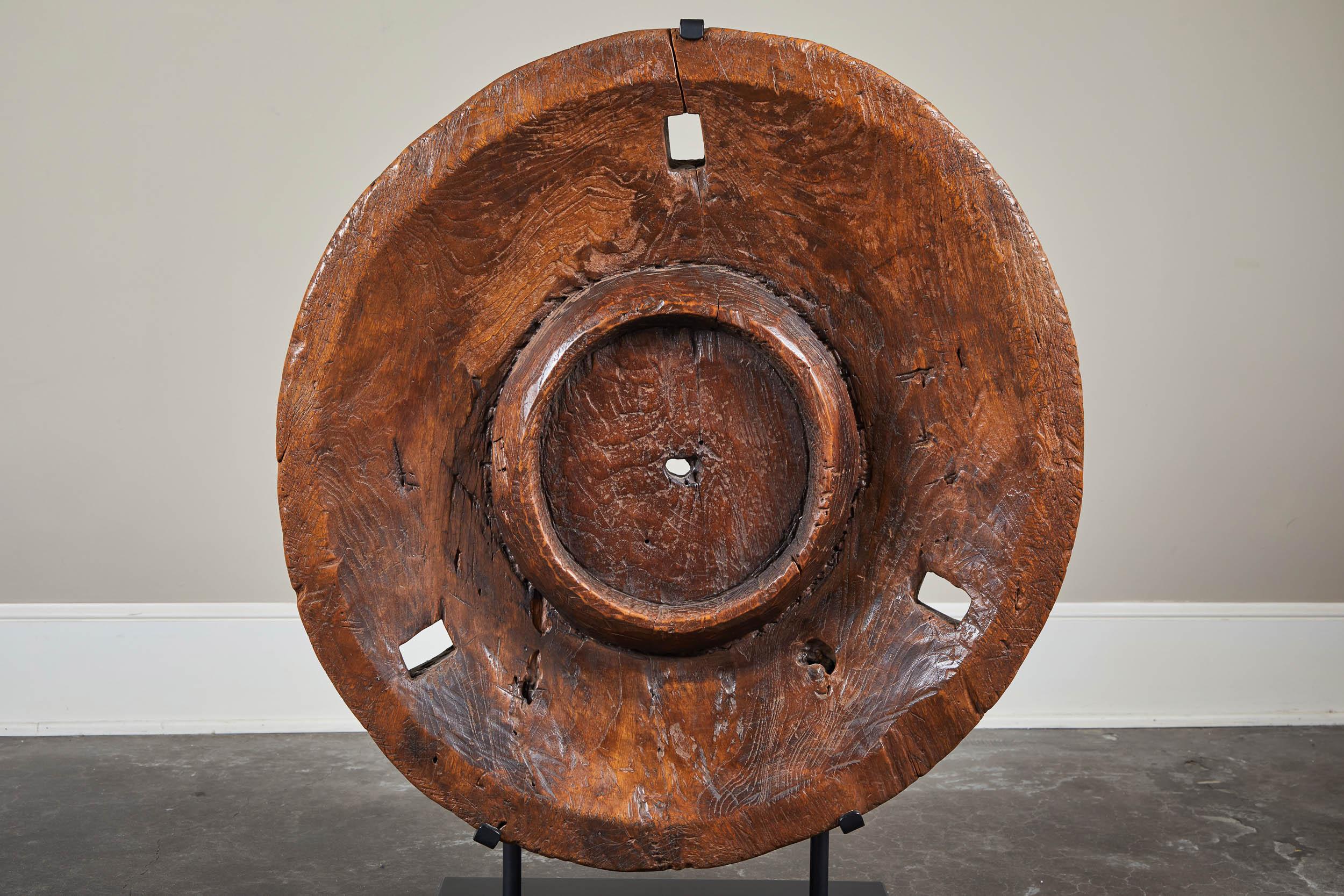 Dense teak granary grinding component with a poetic surface patina of age and wear. Mounting on a custom metal stand for display on tabletop or pedestal.