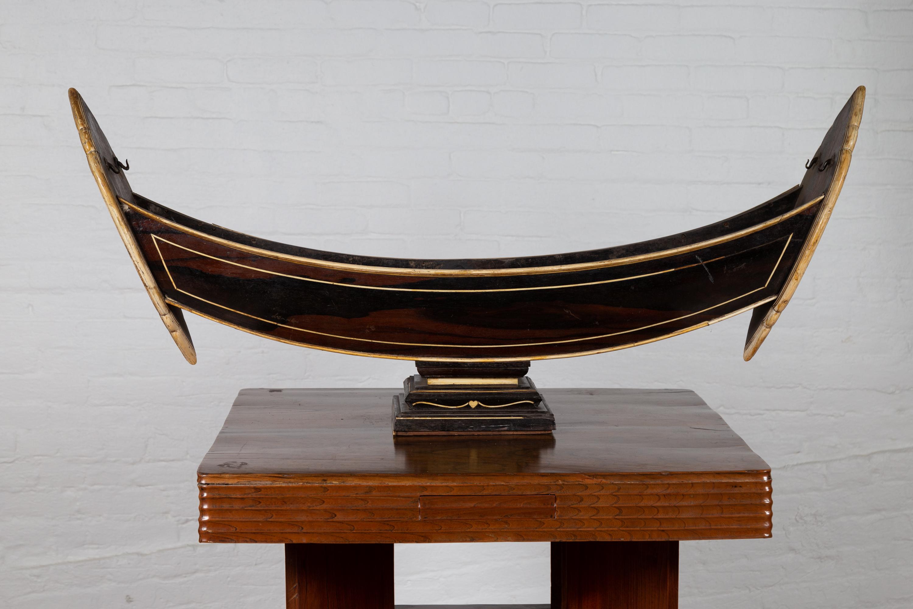 An antique Indonesian handmade boat model on pedestal from the early 20th century, with bone inlay over wood. Born in Indonesia during the early years of the 20th century, this exquisite boat model features a lovely wood finish, accented by a