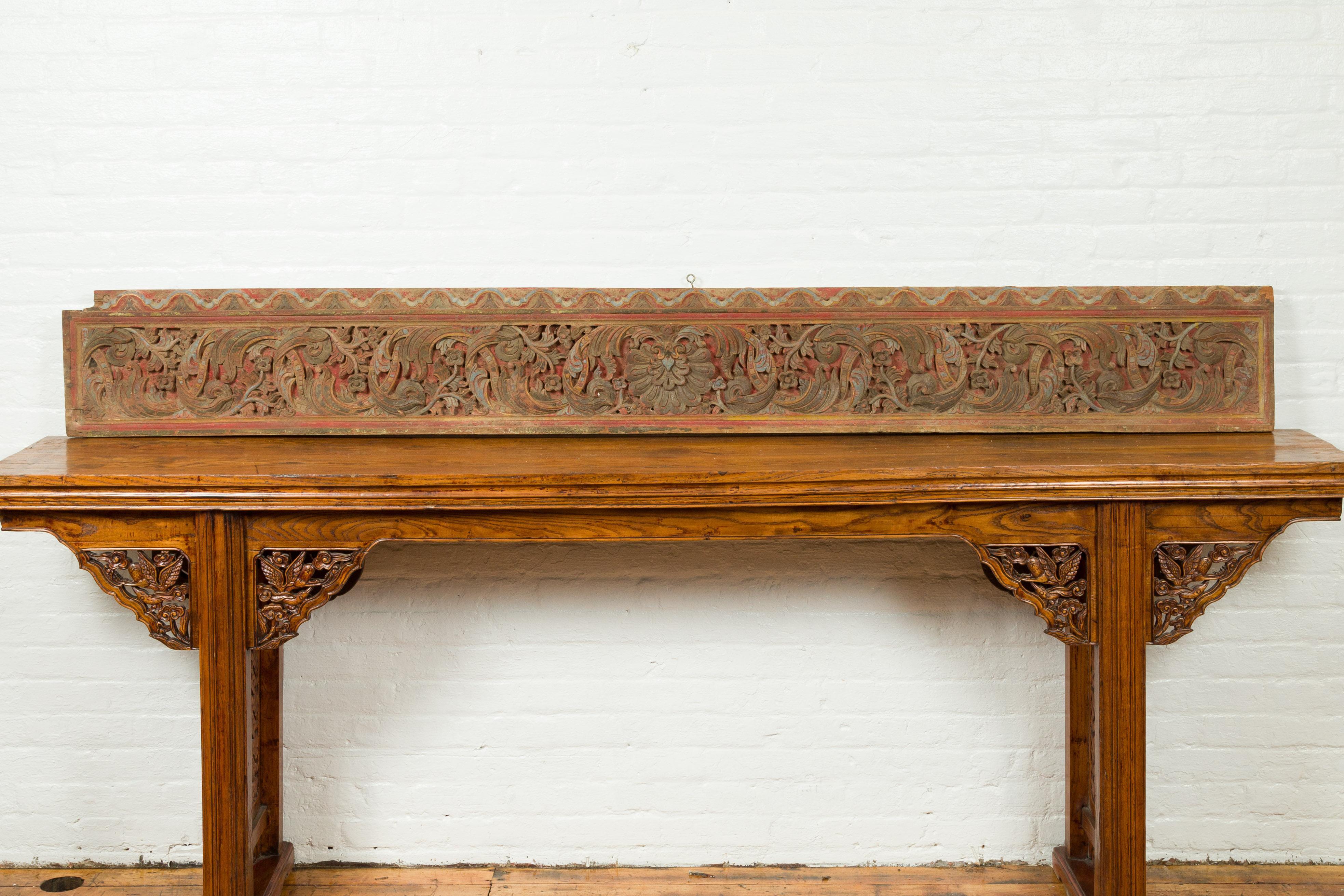 An antique Indonesian carved architectural fragment from a temple, with raised floral motifs. Created in Indonesia for a temple decor, this horizontal architectural panel features a frieze of scrolling rinceaux perfectly accented with green, red and