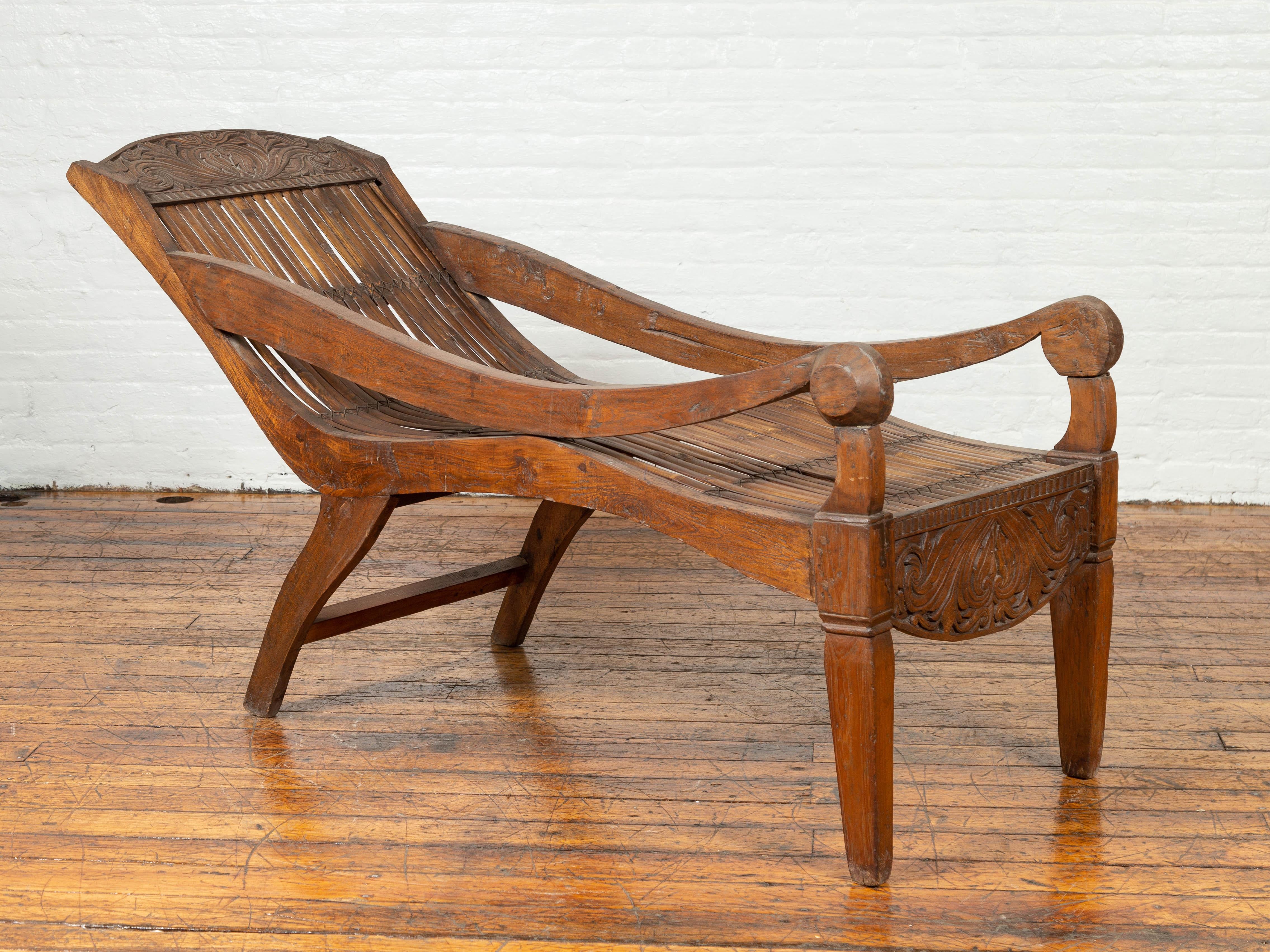 An antique Indonesian reclining plantation lounge chair with bamboo slats and carved motifs. Designed to provide a relaxing experience to the sitter, this Indonesian lounge chair features a nicely curving body with bamboo slats, accented with two