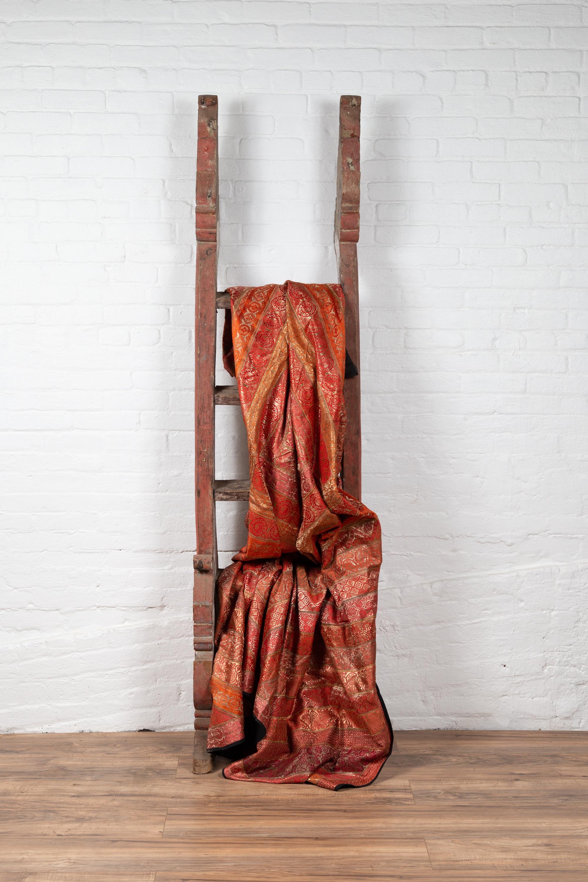 An antique Indonesian red hand carved ladder from the early 20th century, with traces of white and blue accents. Born in Indonesia during the early years of the 20th century, this charming painted ladder will be a wonderful decorative accent in any