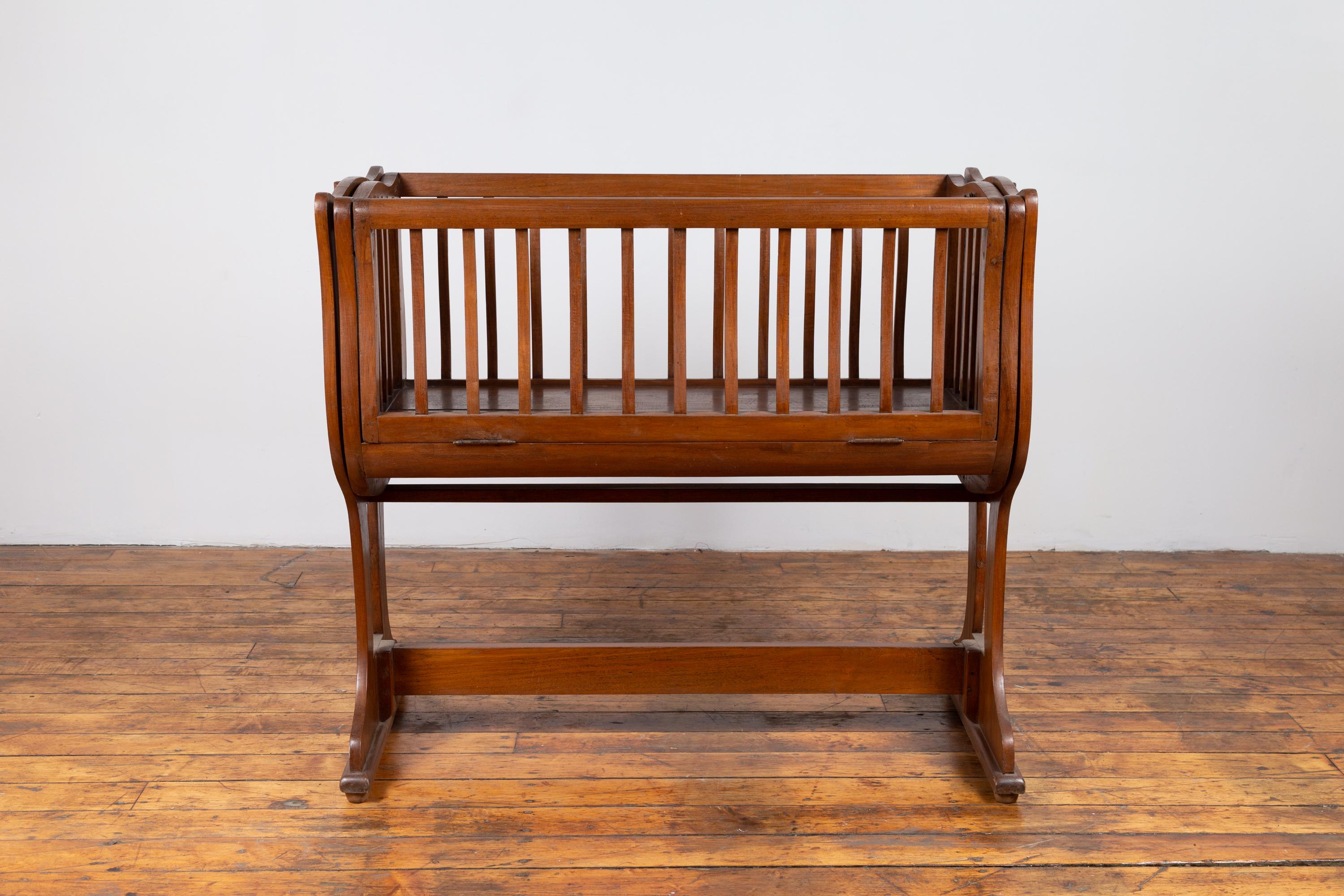 An antique Indonesian baby cradle from the early 20th century, transforming into a one of a kind seat. Born in Indonesia during the early years of the 20th century, this exquisite wooden baby cradle is raised on a trestle base. Rocking from side to
