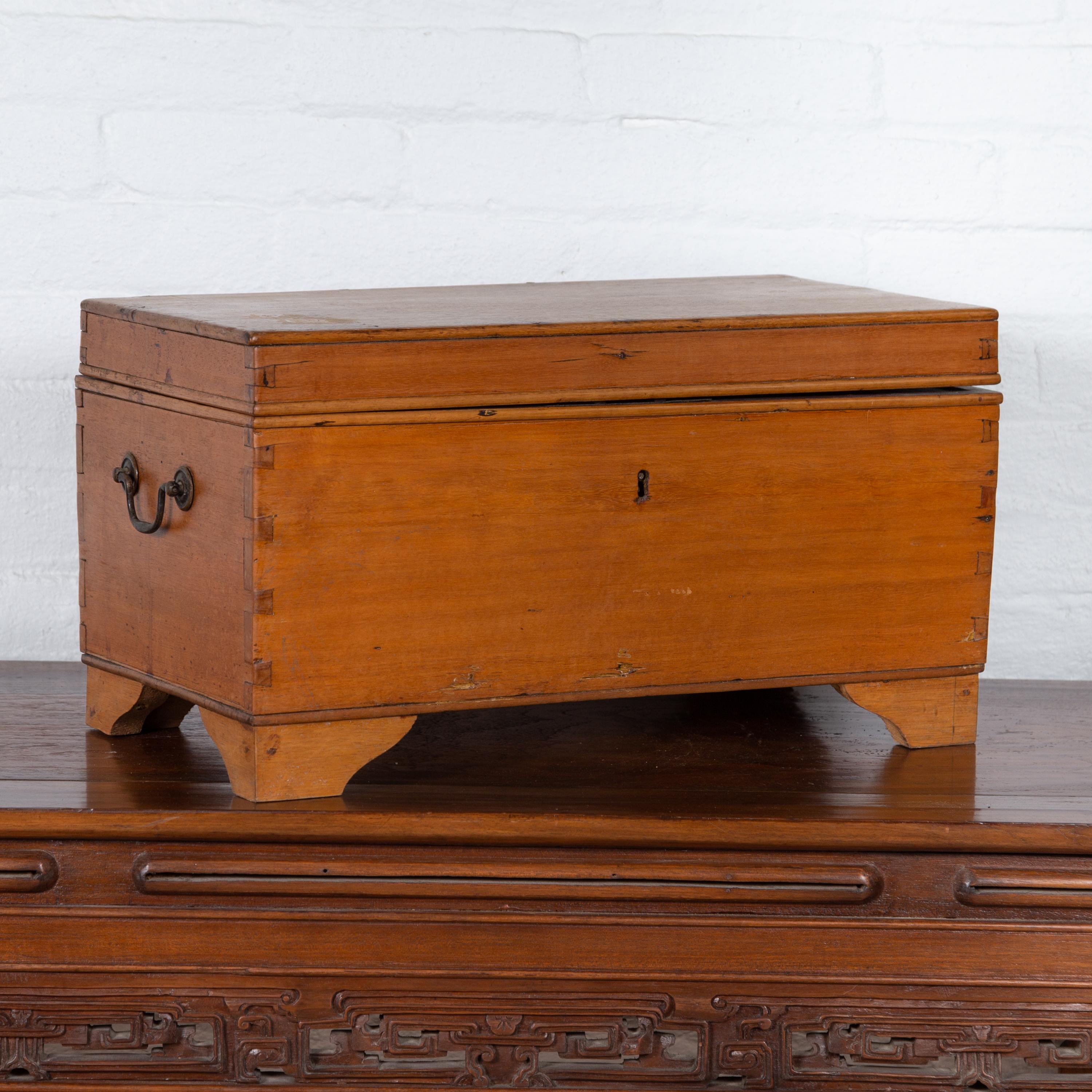 An Indonesian antique wooden decorative box from the early 20th century, with red lacquered interior lid, lateral handles and bracket feet. Created in Indonesia during the early years of the 20th century, this charming wooden box features a linear