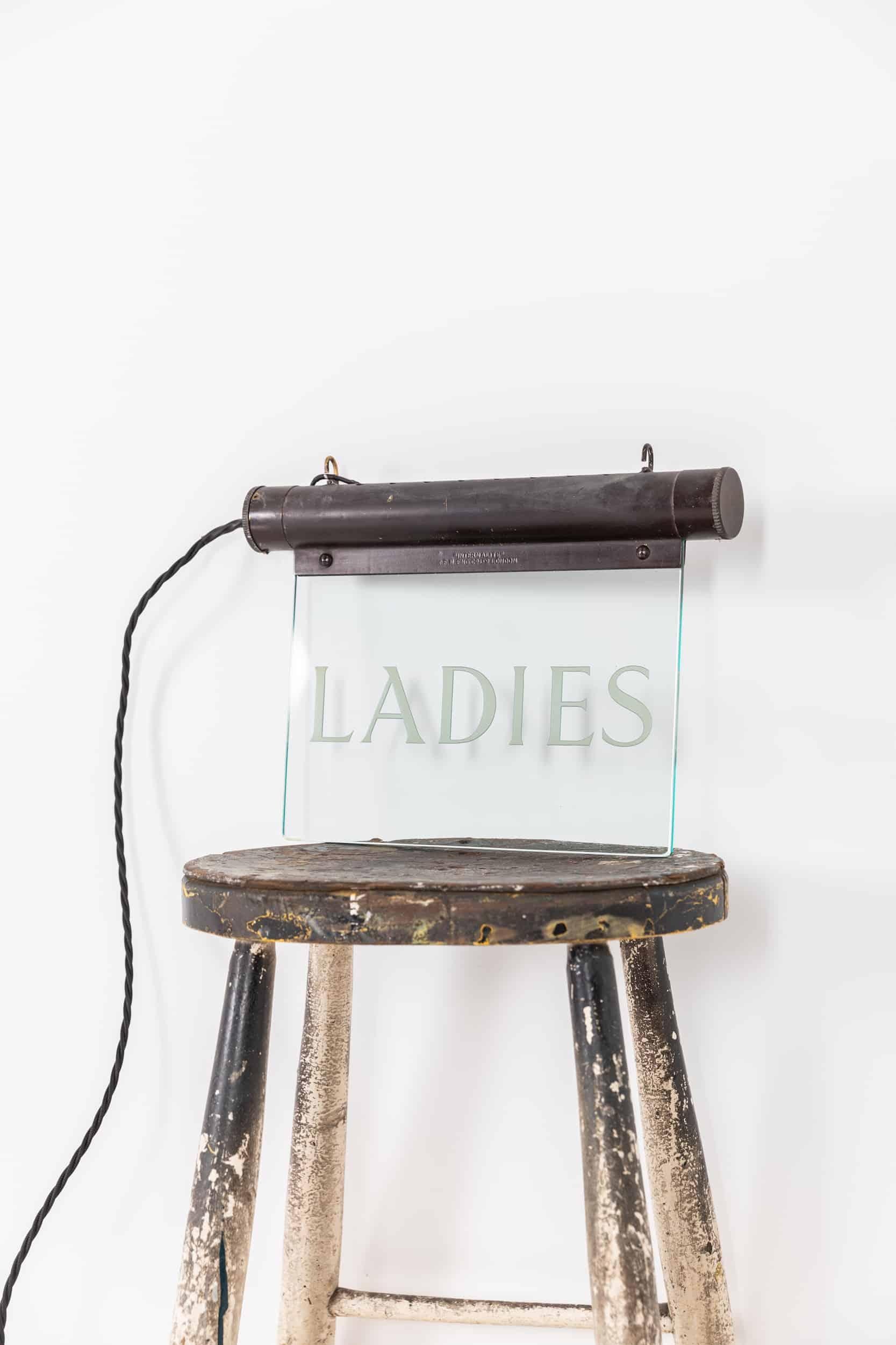 A stunning illuminated 'Internalite' directional sign made in England by K.F.M Engineering. c.1920.

Brass frame, darkened by age, housing the internal illuminations above polished plate glass etched with 'Ladies'. Frame stamped with makers