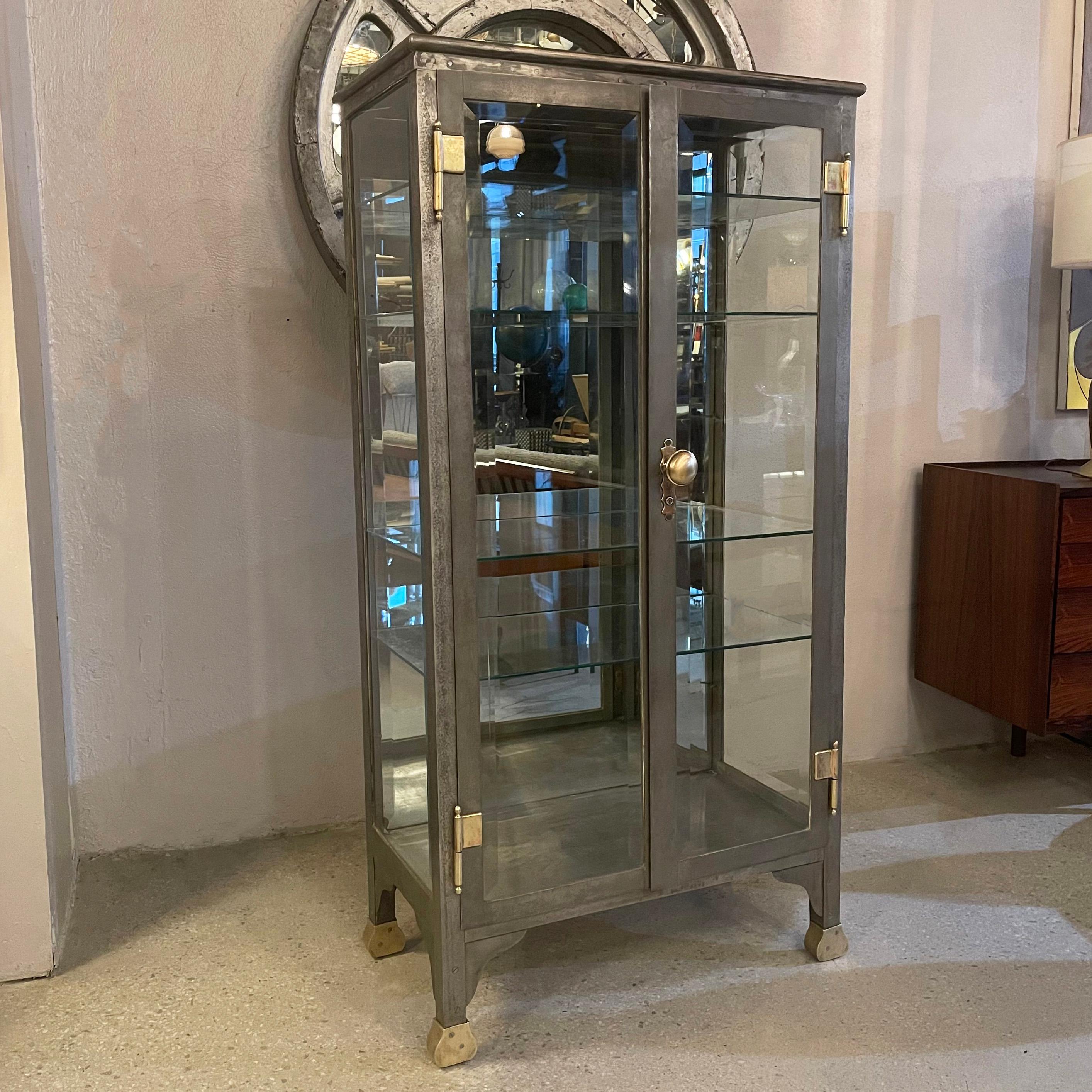 Exceptional, antique, double door, apothecary display cabinet features a patinated brushed steel finish inside and out with brass accents. The cabinet circa 1880's has beveled glass on three sides and mirror interior backing with four glass shelves