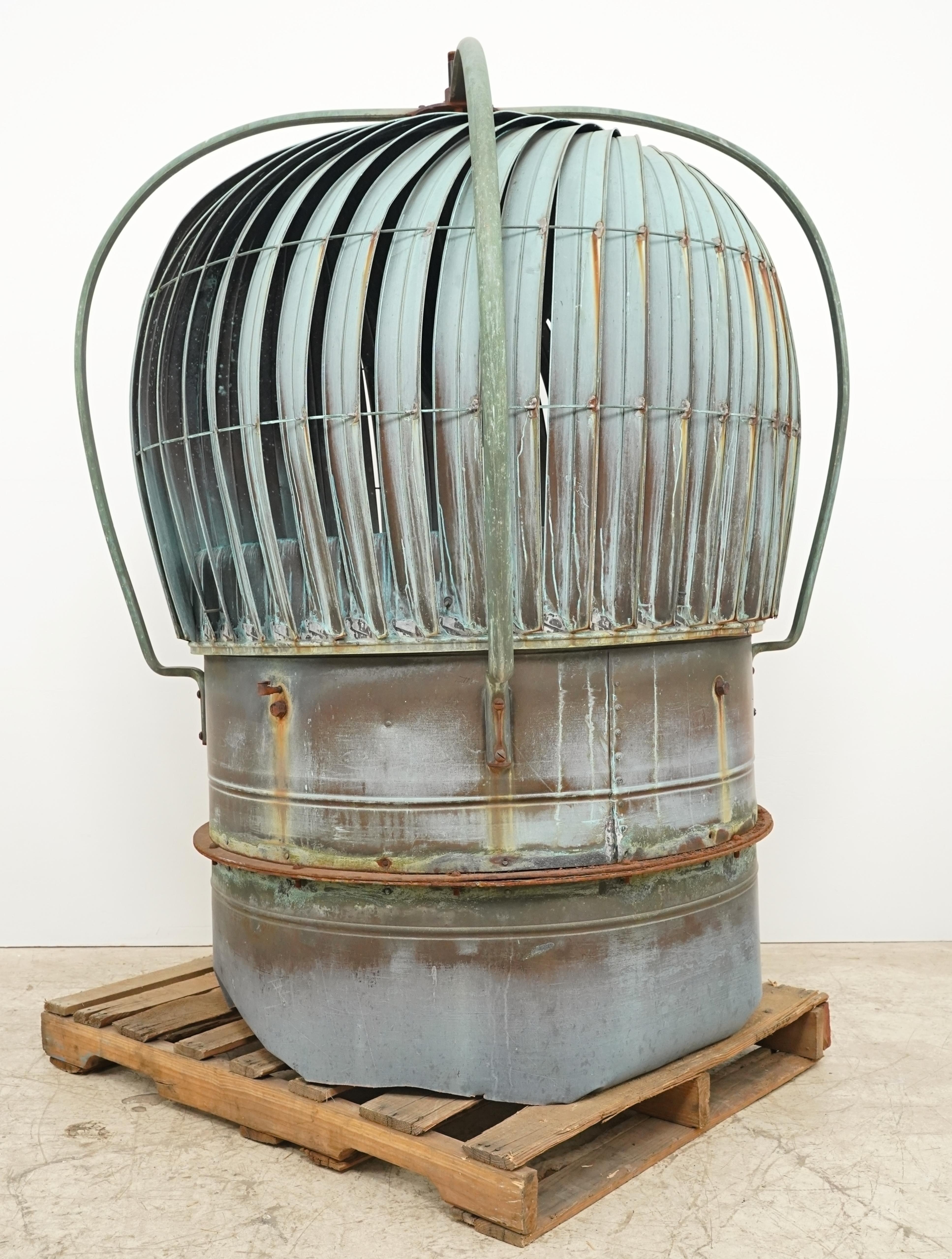 Reclaimed large roof turbine ventilator made of an all-copper exterior with minimal steel framing on the interior. It features a series of curved blades enclosed within a cagelike structure, all mounted on a cylindrical base. It's designed to expel