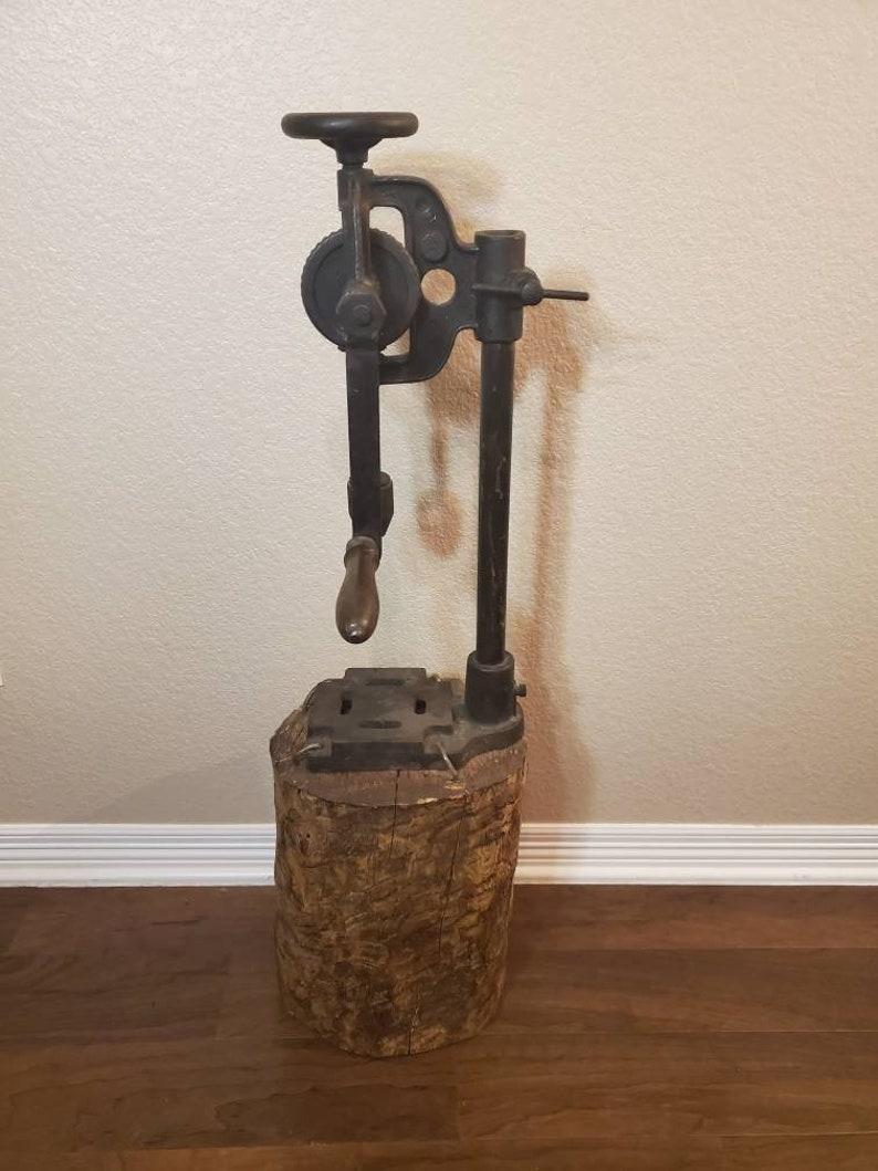 A rare antique industrial hand crank iron blacksmithing farmer barn post or bench drill press mounted on large wooden stump log base. Rustic, carved, chopped and loaded with rustic character and patina. 

This early 20th century American antique