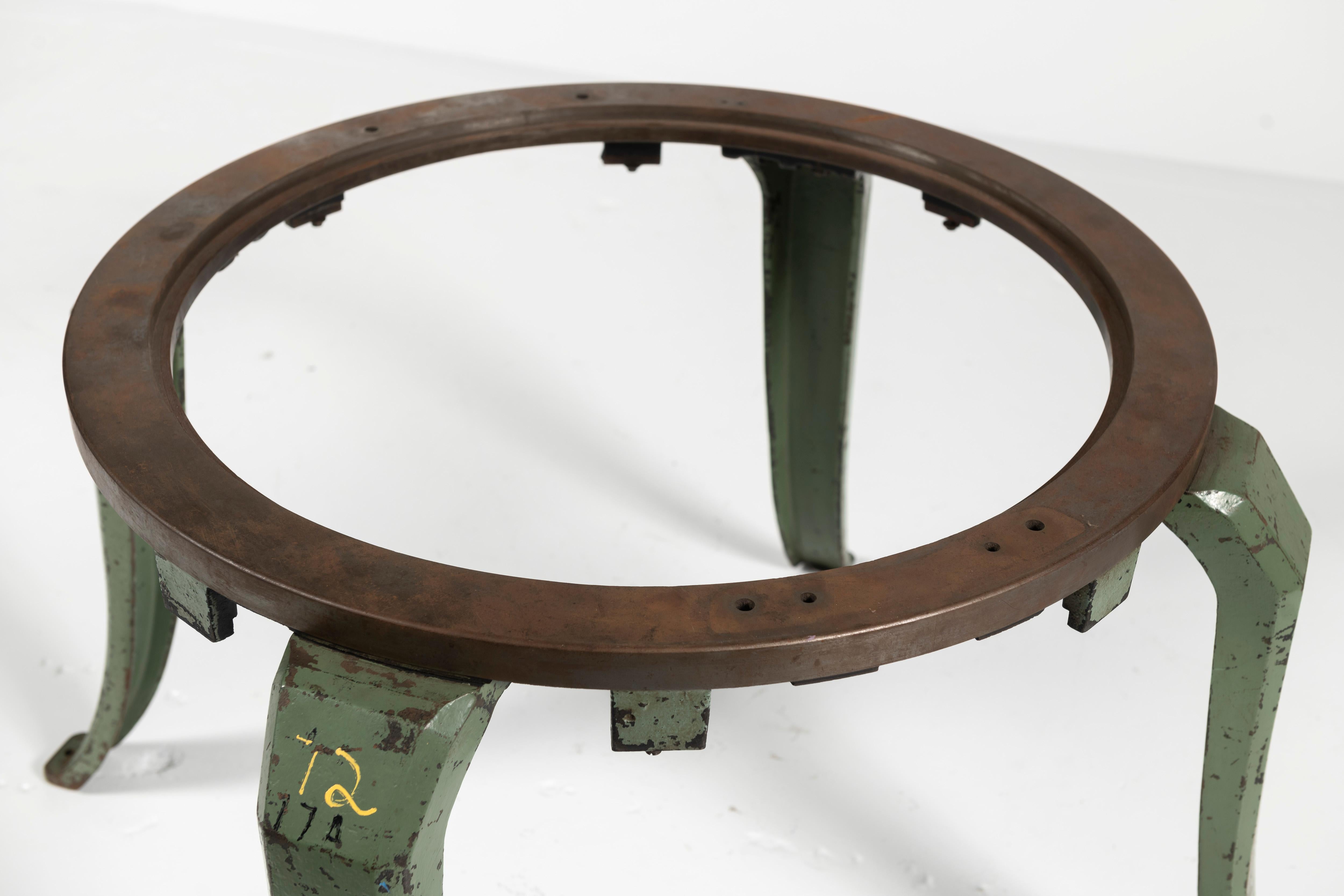 This collectible cast iron industrial machinery piece that has been converted from its original use to a table base. The table is round with beautifully curved legs. The cast iron has aged perfectly, with oxidation and some chipped industrial green