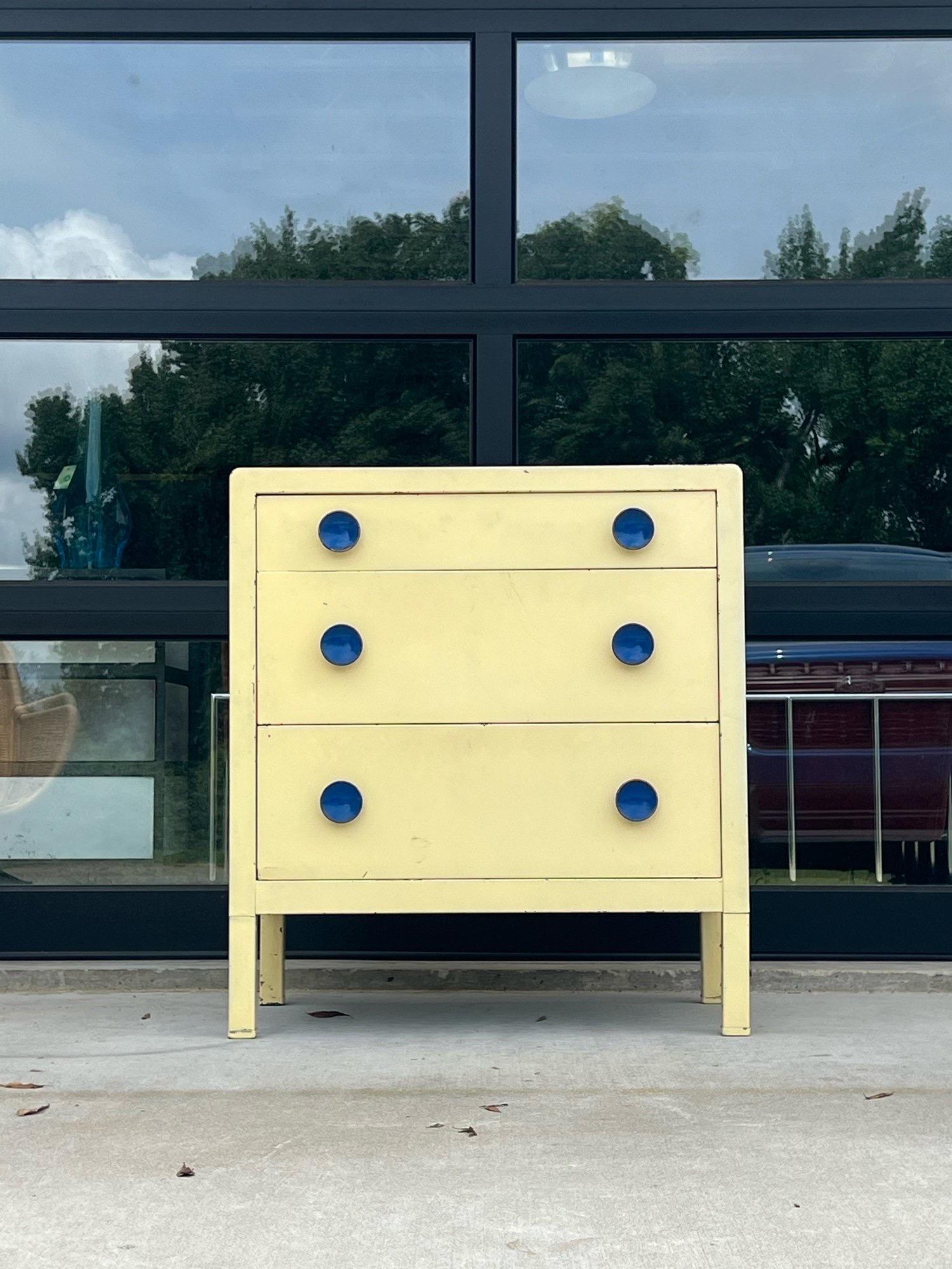 If you’re looking for a very cool industrial antique with nice patina then this is the one. A steel three drawer dresser designed by industrial designer Norman Bel Geddes. A very nice collectible piece with bright blue sculpted pulls and cream metal