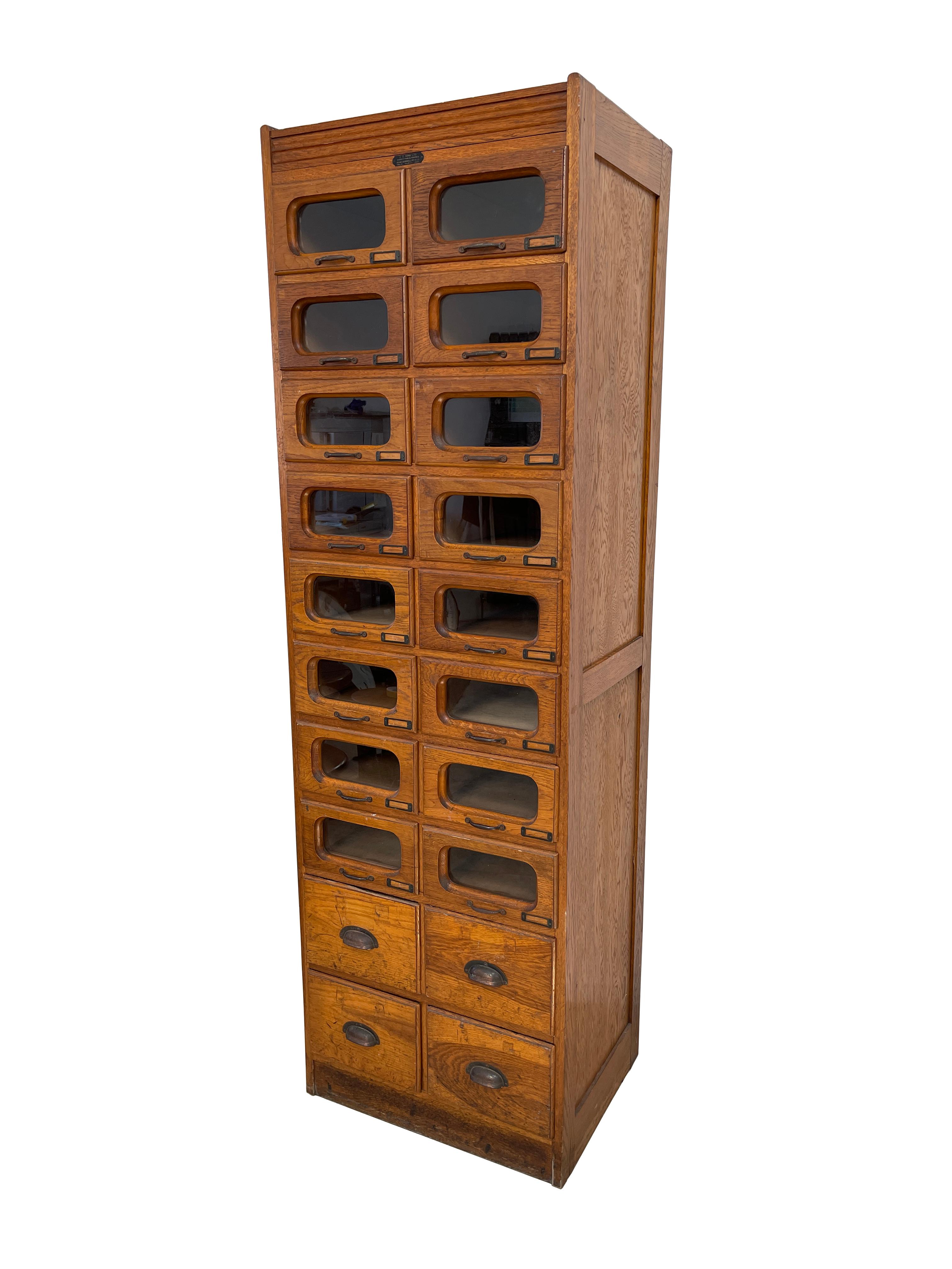 - A beautiful set of tall oak haberdashery drawers, circa 1930. 
- The cabinet is marked by illustrious manufacturers 'J. C. KING LTD. Shopfittings & Sundries 42-60, Goswell Rd, E.C.I. TELE, CLERK. 2317'.
- A total of 16 glazed drawers with