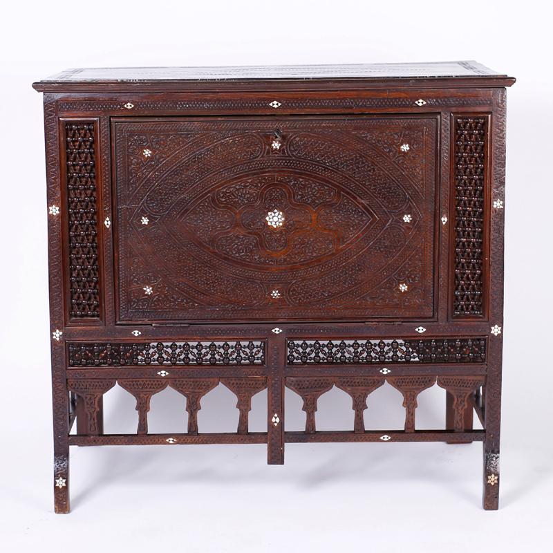Antique cabinet with a fold down door in front and blanket chest in the top. Crafted in mahogany and featuring elaborate carvings highlighted with bone inlaid flowers, stick and ball panels, Moorish arches around the skirt and unusual dog legged