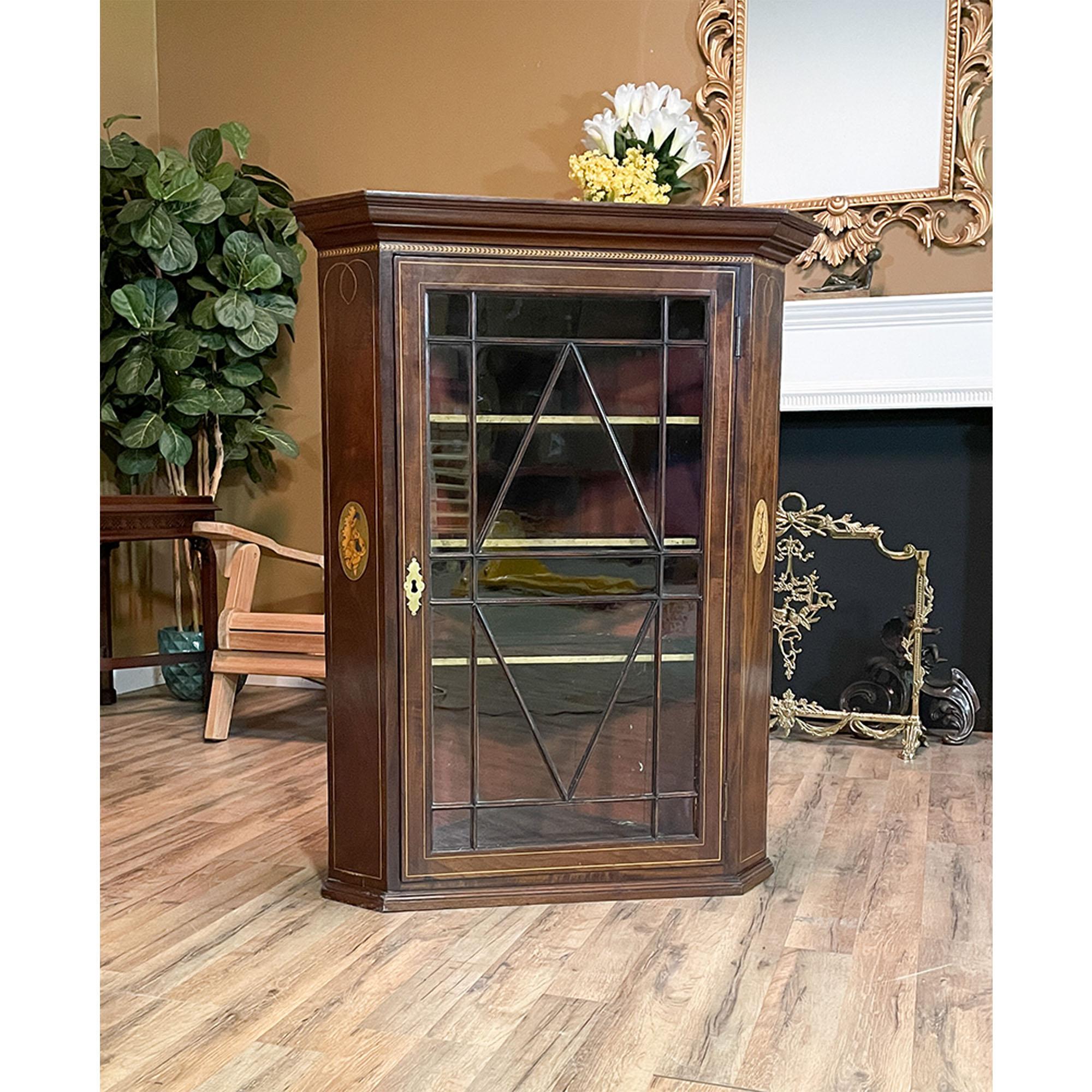 An Antique Inlaid Hanging Mahogany Corner Cabinet. The Antique Inlaid Hanging Mahogany Corner Cabinet features a beautiful carved molding along the top with hand inlaid patterns below. The corner cabinet has individual lattice work in the doors and