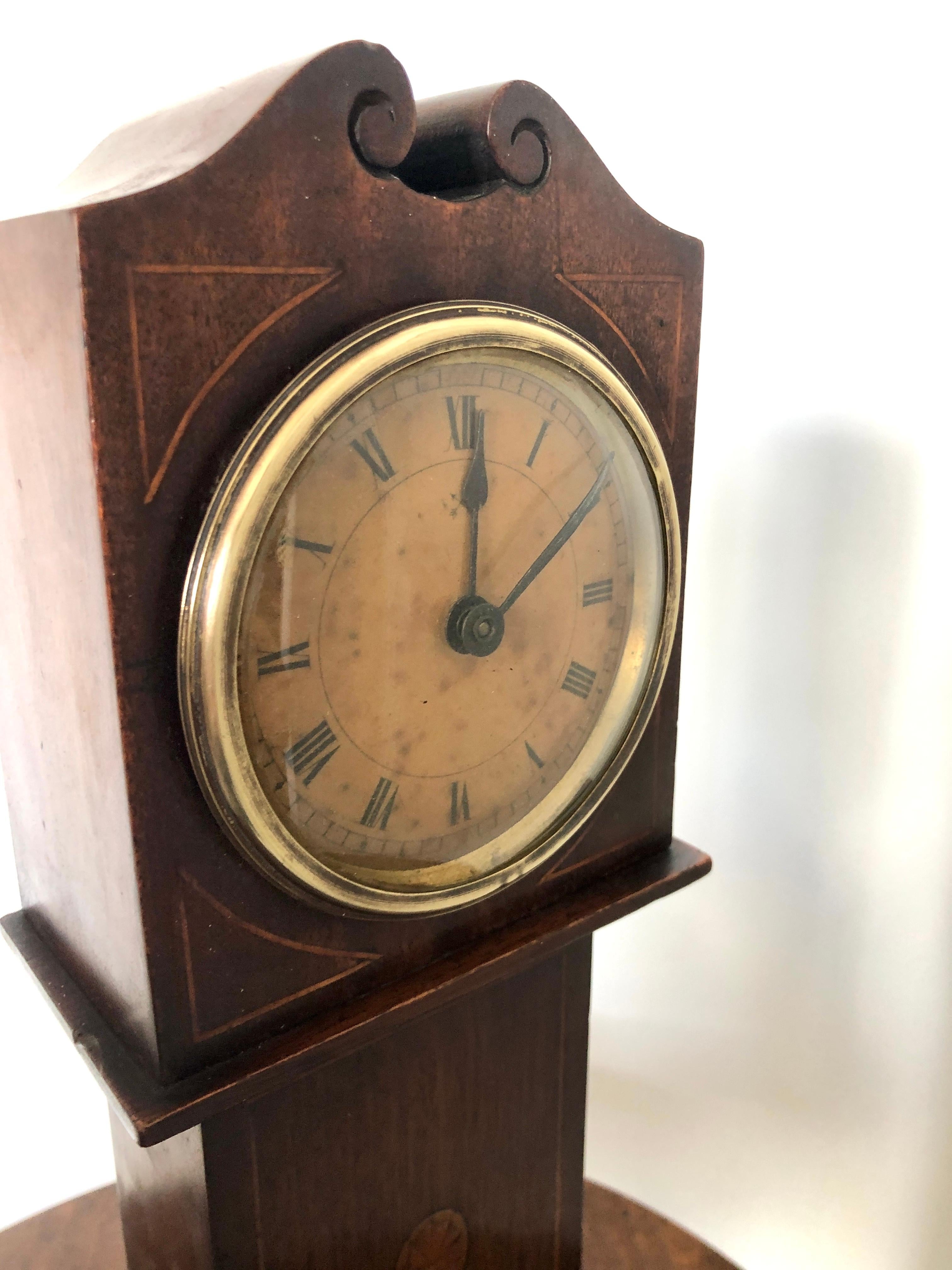 Antique inlaid mahogany apprentice miniature longcase clock having a swan neck pediment above a round dial with a brass bezel and satinwood inlay to the corners, inlaid shell to the centre of the mahogany case and standing on a plinth base.

A