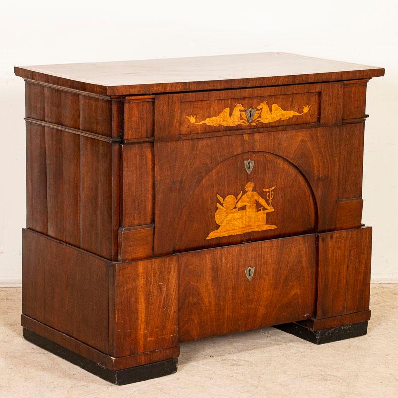 A fine mahogany empire chest of drawers or commode with satinwood inlays. Mythological creatures adorn the upper drawer; when opened, a felt covered surface for writing is revealed along with storage cubbies and even holders for bottled ink. A