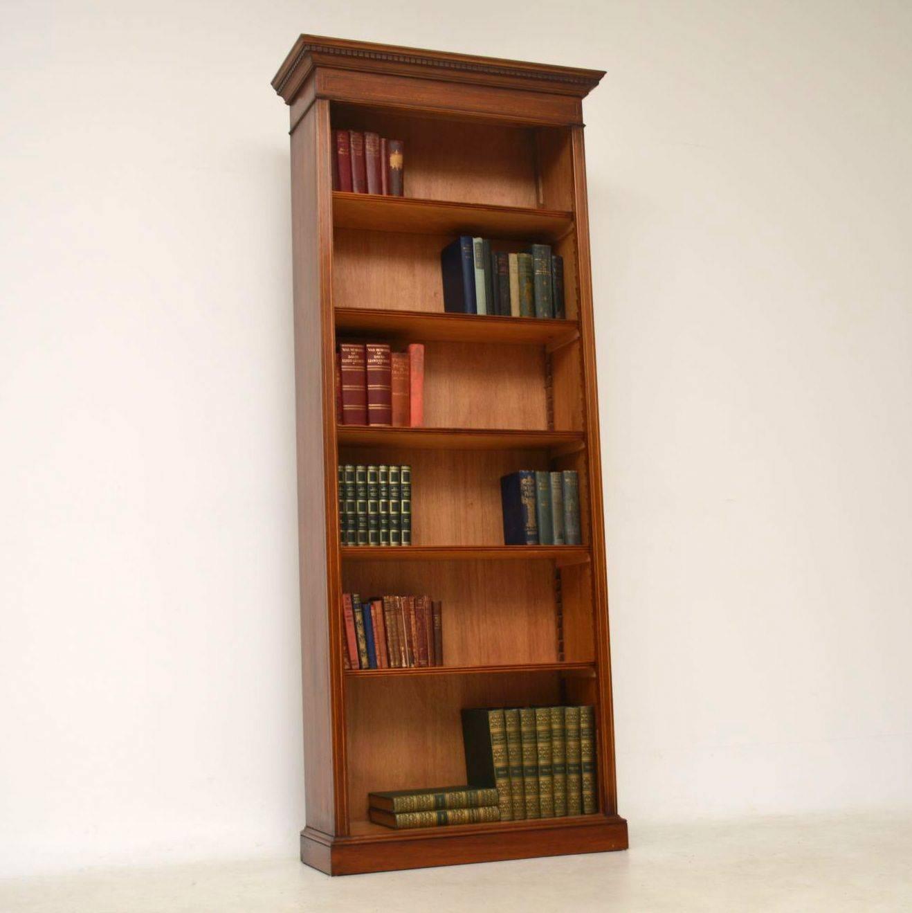 Tall antique Sheraton style open bookcase in mahogany with satinwood inlays. It has five shelves with reeded fronts that are all adjustable on sharks teeth supports. The top cornice has dental mouldings below and this bookcase sits on a plinth base.
