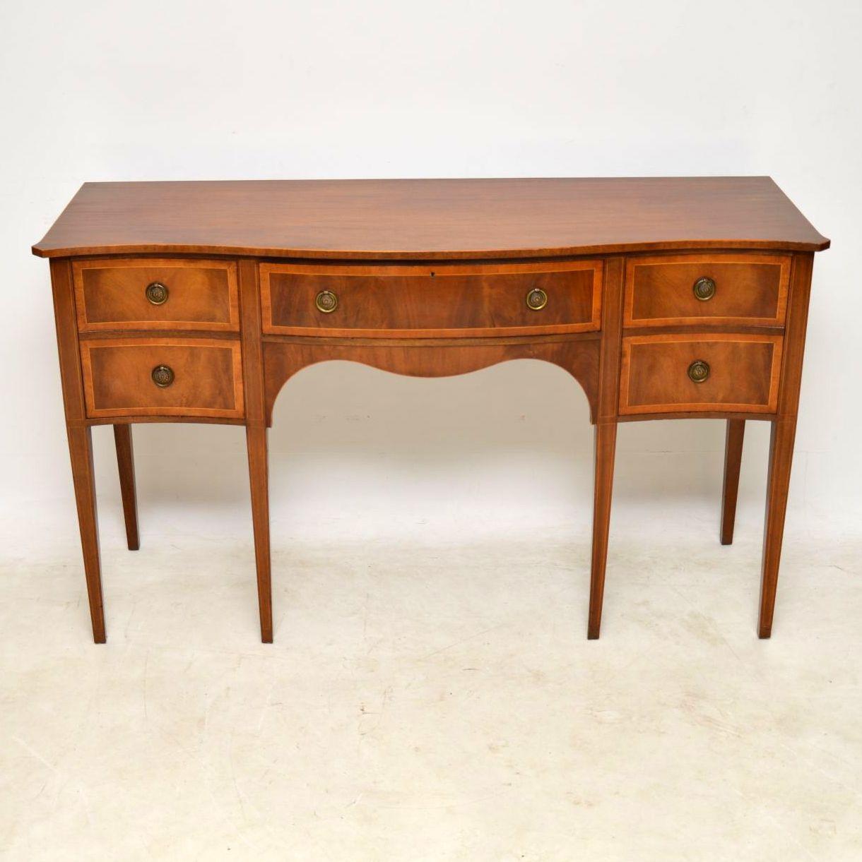 Antique Sheraton style mahogany sideboard in excellent condition and dating from about the 1950s period. It has a serpentine shaped front with dummy drawers on either side that are really cupboards and a proper drawer in the middle. There’s fine