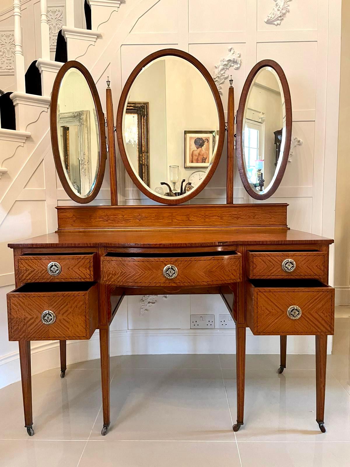 Fine antique inlaid satinwood dressing/vanity table having delightful stringing inlay throughout the entire satinwood piece. It boasts three oval tilting beveled edged mirrors with pretty oval inlaid satinwood frames supported by inlaid uprights