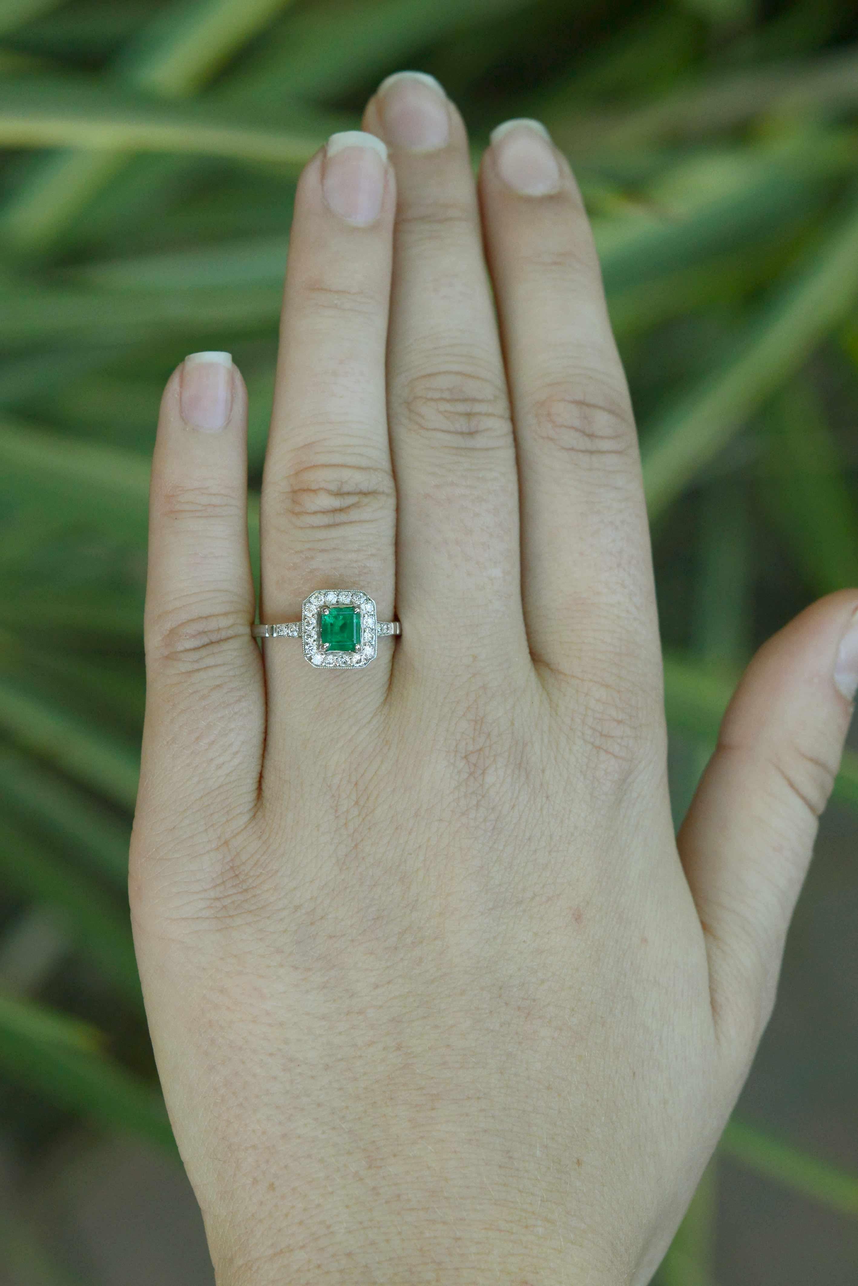 A glowing, deep green Colombian emerald takes center stage in this striking Art Deco style engagement ring. Secured in hand-fabricated platinum and surrounded with a dainty halo of sparkling, round cut diamonds in a sleek, geometric style that sits