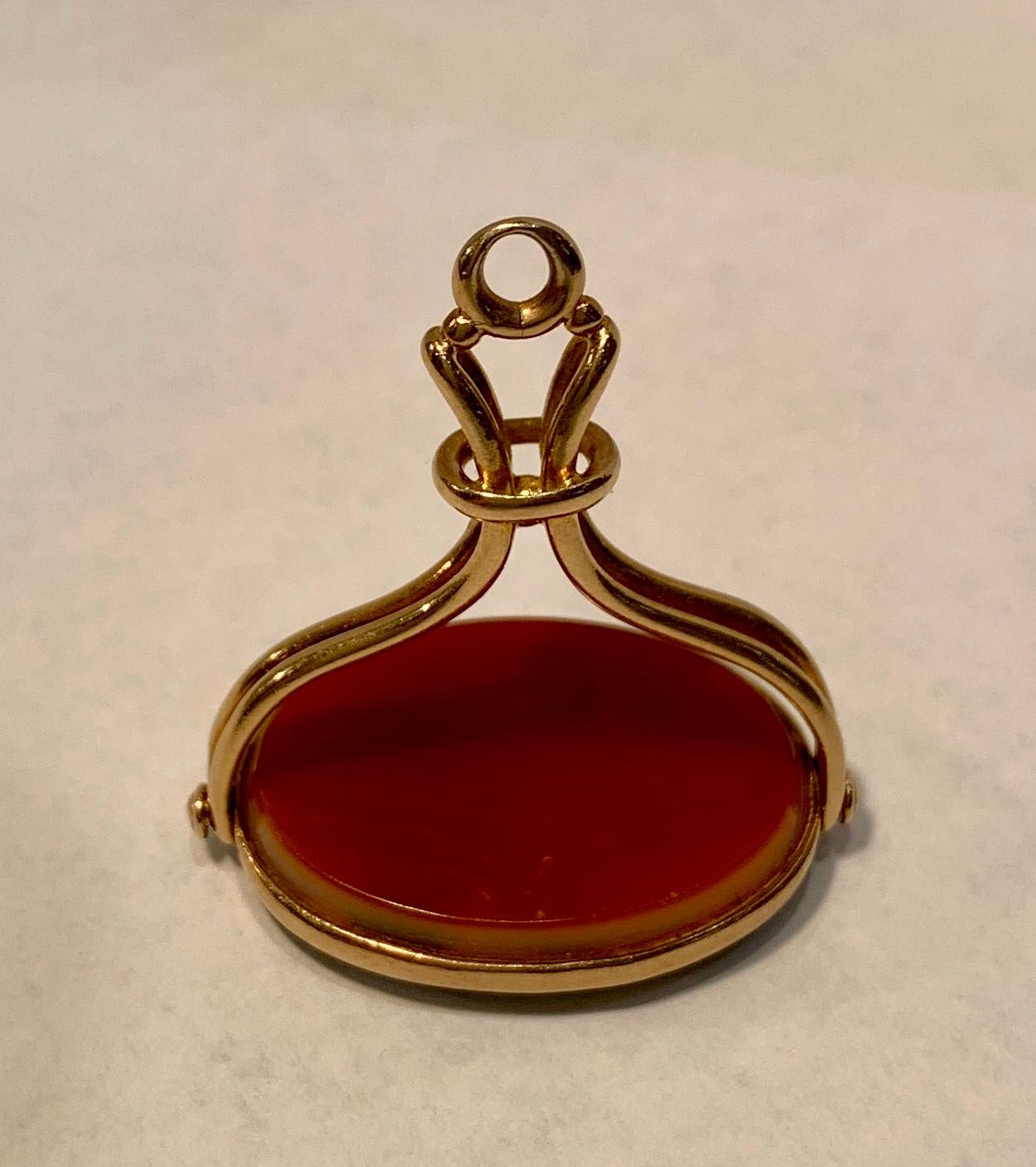Antique 1850s, early Victorian intaglio spinner fob pendant features a reversible, revolving, beveled oval slice of translucent carnelian on one side and translucent black agate on the other side. The carnelian and agate stones are bezel set in 14