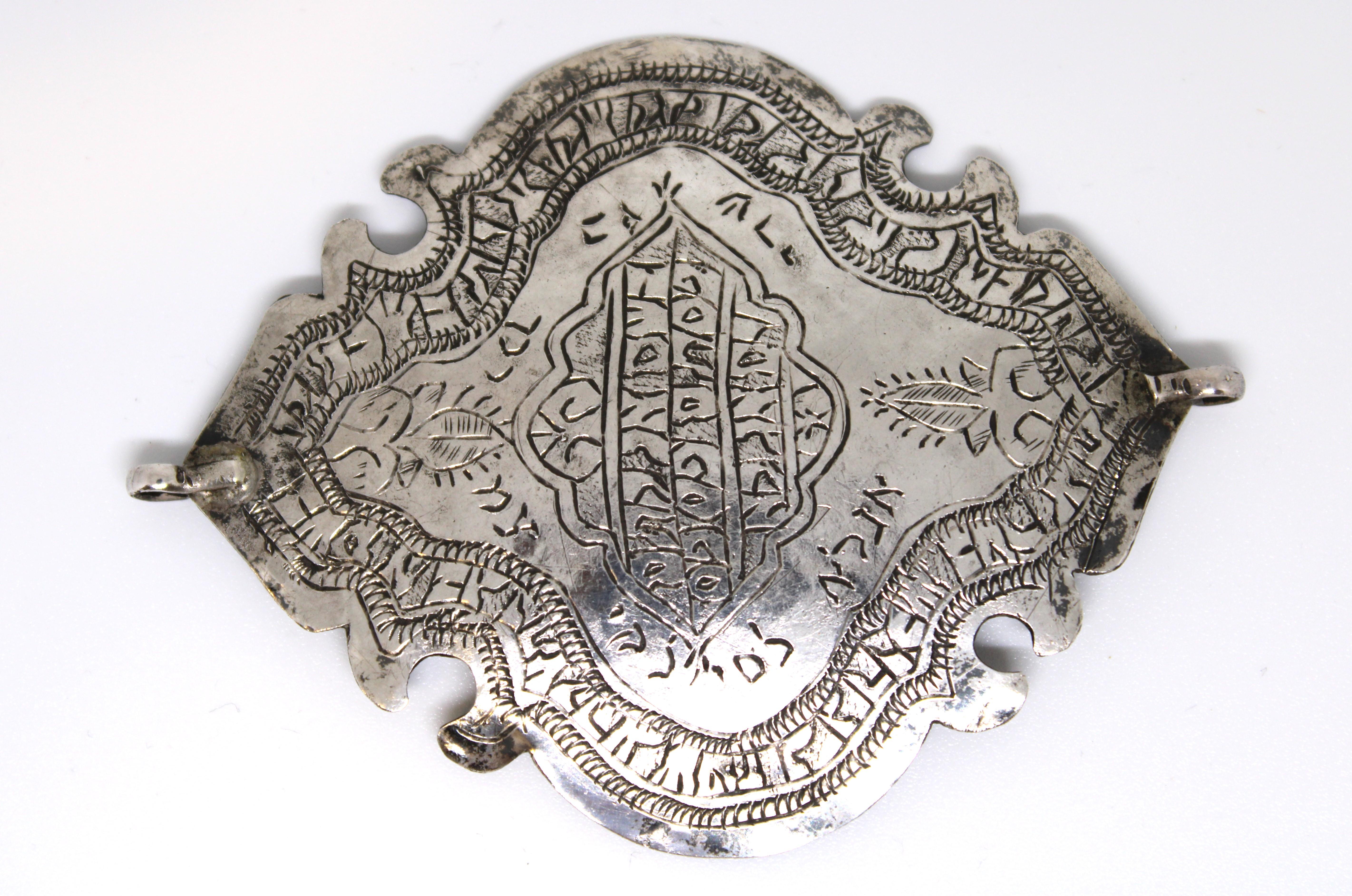 Cette exceptionnelle amulette ancienne en argent provenant d'Iran illustre l'artisanat raffiné et la profondeur spirituelle de l'héritage juif persan. Formée d'un élégant losange lobé aux contours délicats, l'amulette est gravée de détails