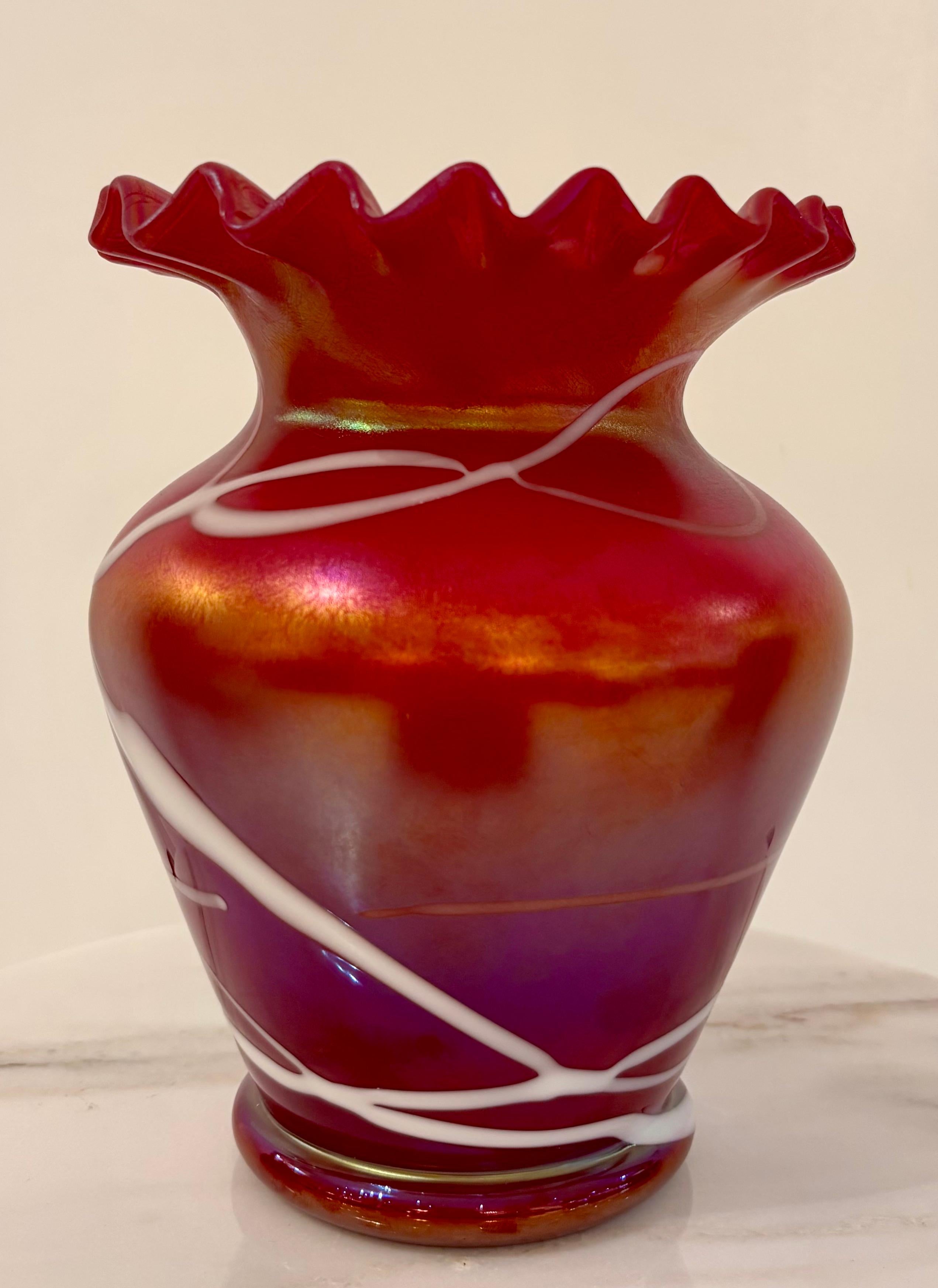 A stylish and luminous iridescent art glass vase by Wilhelm Kralik Sohn, Bohemia, circa 1900. This handblown piece features a vibrant cranberry-to-amethyst ground, richly accented by applied white threading in a pulled ribbon motif. Its bold ruffled