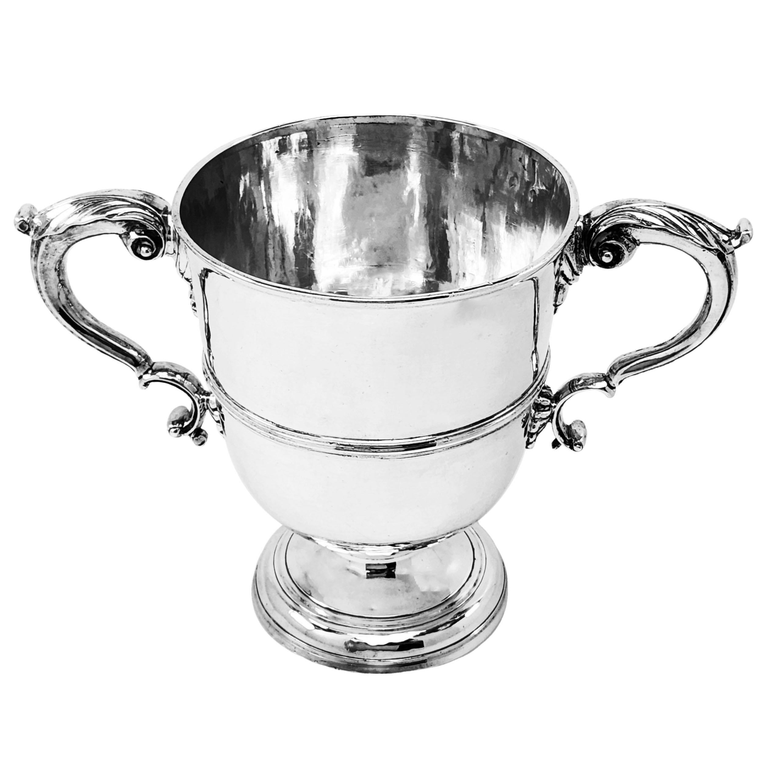 A classic Antique Irish George II Cup with a pair of impressive acanthus leaf topped scroll handles. The Georgian Cup has a band around the body and an engraved crest on the one side. The Cup stands on a spread pedestal foot. This 18th Century Irish