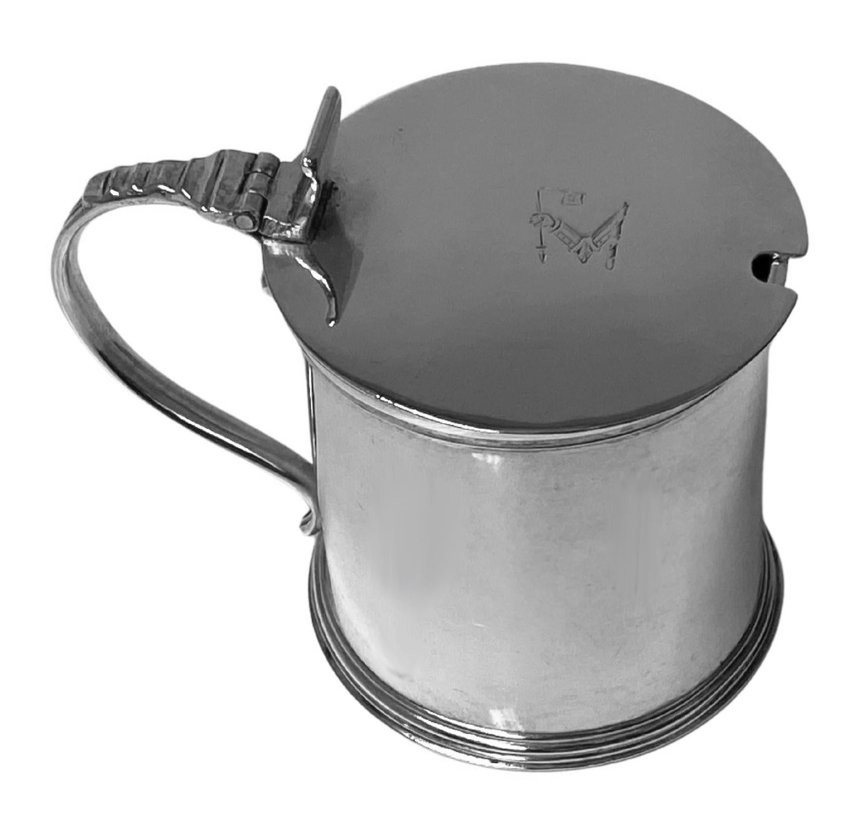 Antique Irish Georgian silver mustard pot Dublin 1824 William Nolan. Cylindrical drum shape, plain body, scroll reed and strap design handle. Engraved on cover with crest of arm and hand grasping a flag. Fully hallmarked on underside and monarchs