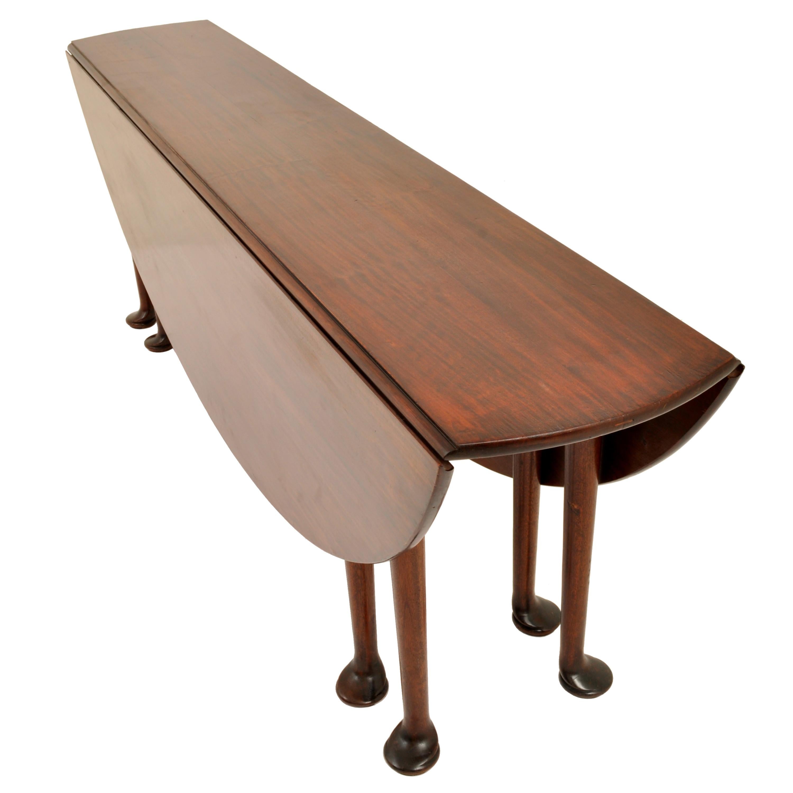 A fine and large Georgian mahogany wake or harvest table, circa 1760. The long table of drop-leaf and gateleg form, made of solid figured mahogany, having eight robust legs with substantial pad feet. The table having demilune drop leaves, each