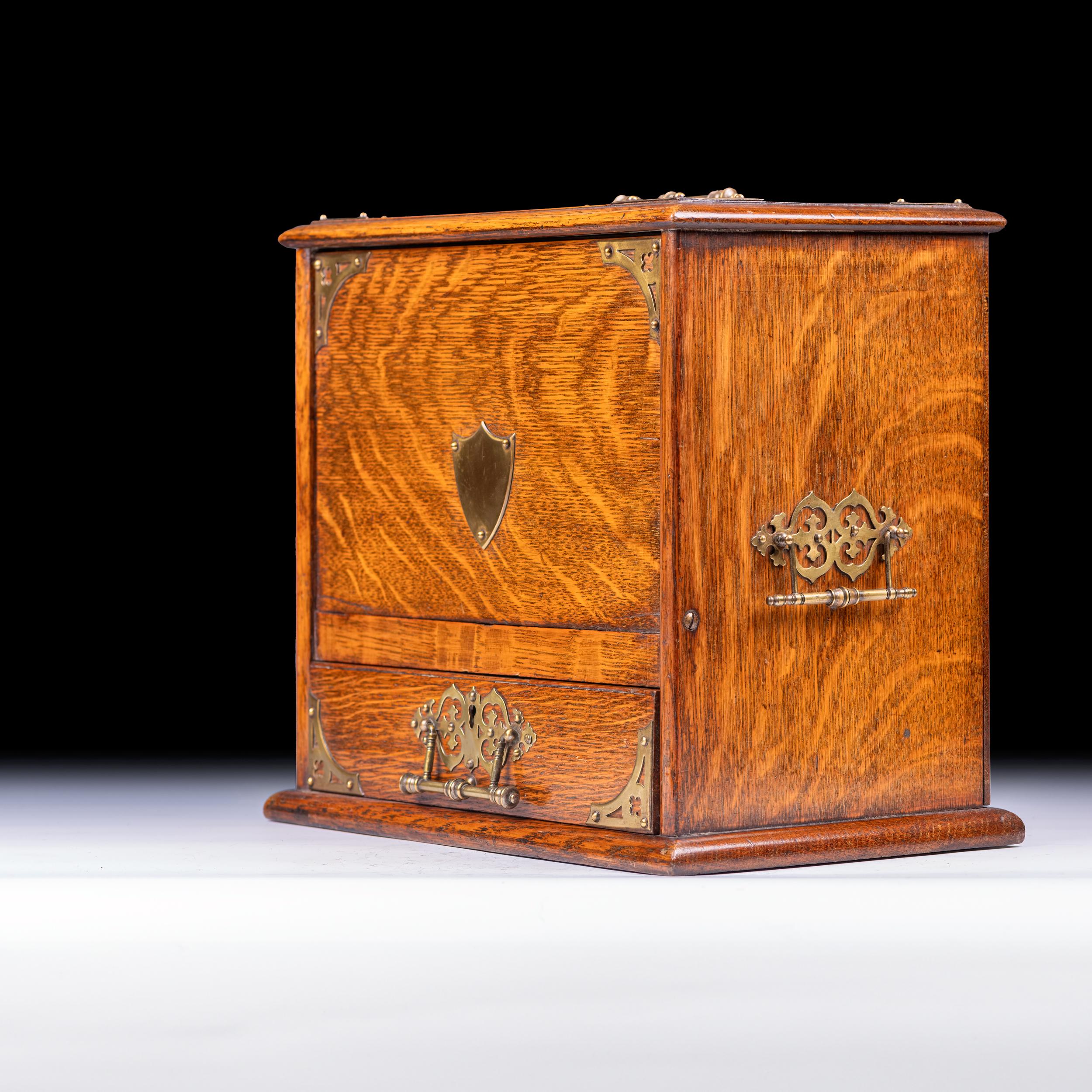 A good Antique oak and brass bound stationary metamorphic letter box, of rectangular outline the shaped top with brass carrying handle above a hinged compartment fitted for stationery, the base with one long drawer, fitted for pens and inkwell on
