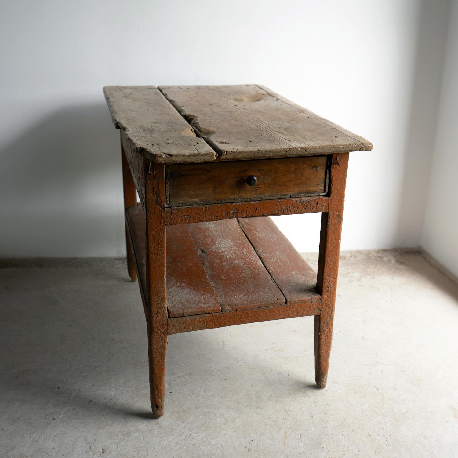 ANTIQUE SIDE TABLE

A decorative and rustic piece constructed of pine with square tapered legs united by a box stretcher with a frieze drawer and a shelf underneath the two-plank top.

Layers of original paint, the top layer being a burnt orangey
