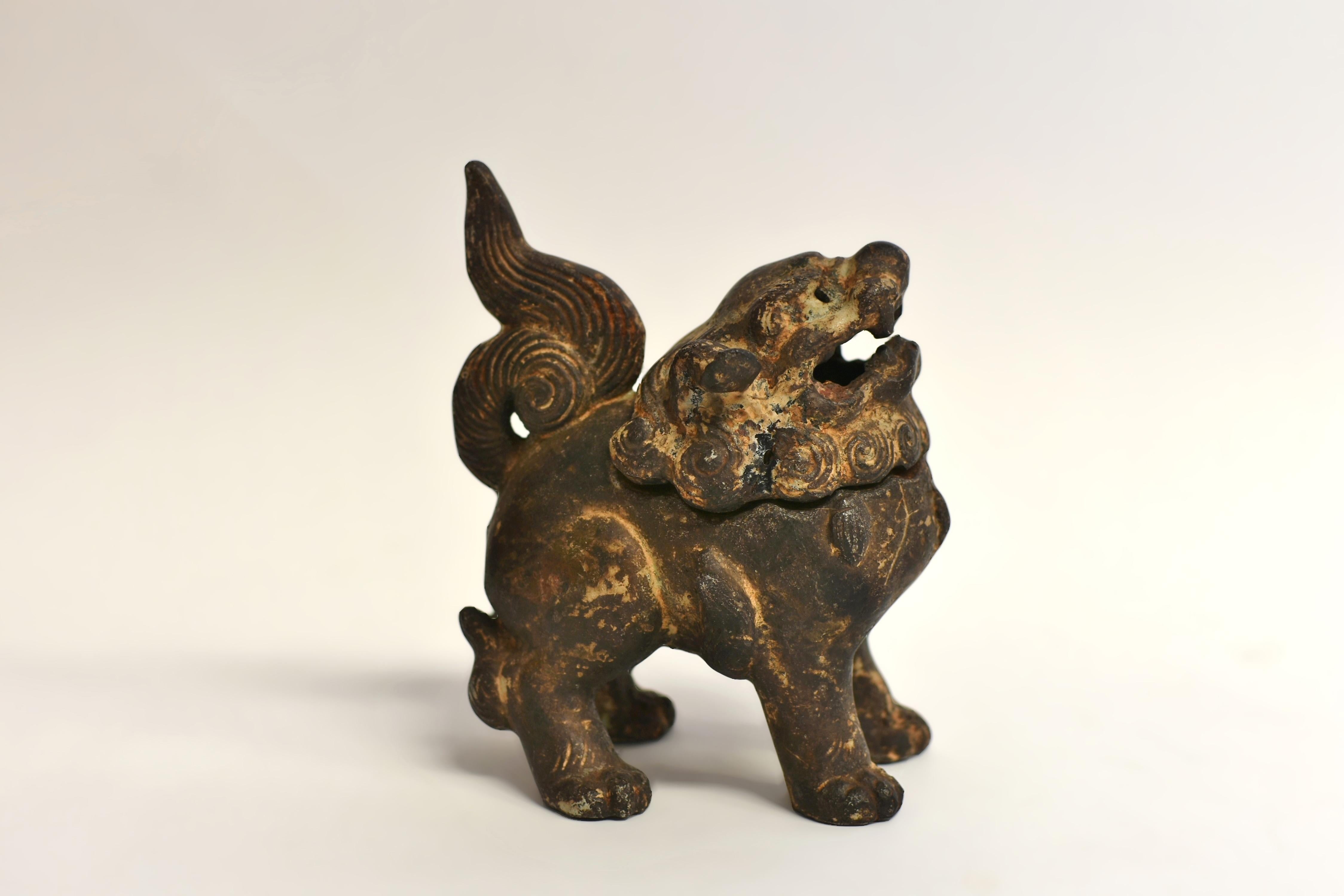 An original 19th century iron foo dog incense burner. Well-fashioned in a standing position, wearing a collar decorated with bells. The large head with open jaws and curly eyebrows, framed by a curled mane. The body masculine with all four legs