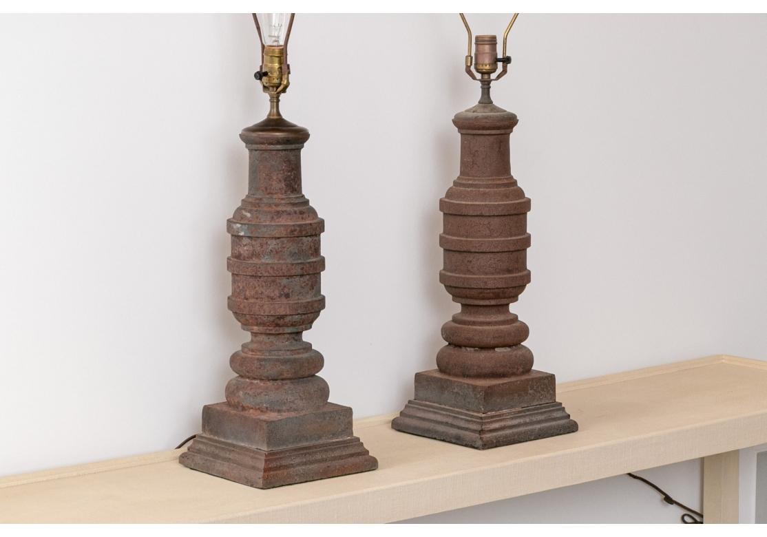 Pair of heavy rustic iron lamps purchased from Yellow Monkey Antiques, having a baluster form, three concentric bands around the standard and resting on a tiered square base. The top with a fleur-di-lis finial.

Dimensions: 8