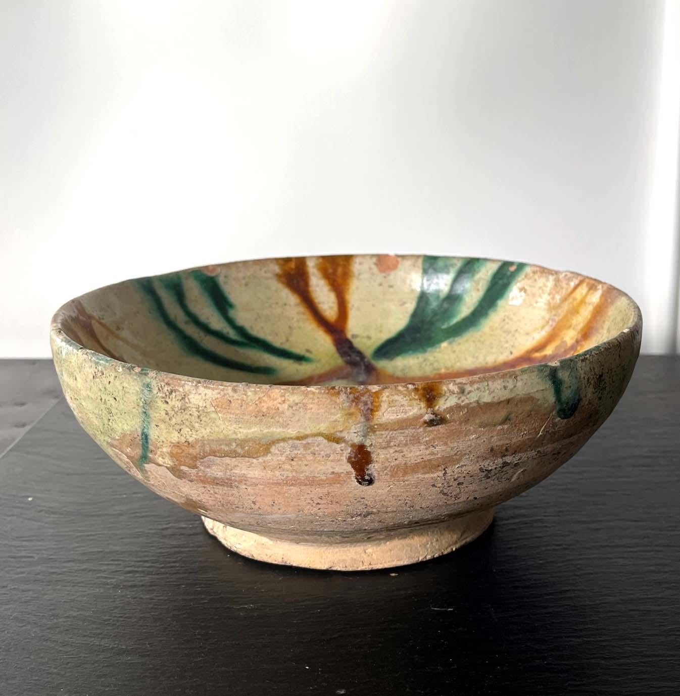 An Islamic ceramic bowl from Samanid Dynasty Persia circa 10th century, possibly from Nishapur. The earth ware body of the bowl was made of a red clay, which was covered with an overall cream white glaze. On top of the glaze, amber yellow, and green
