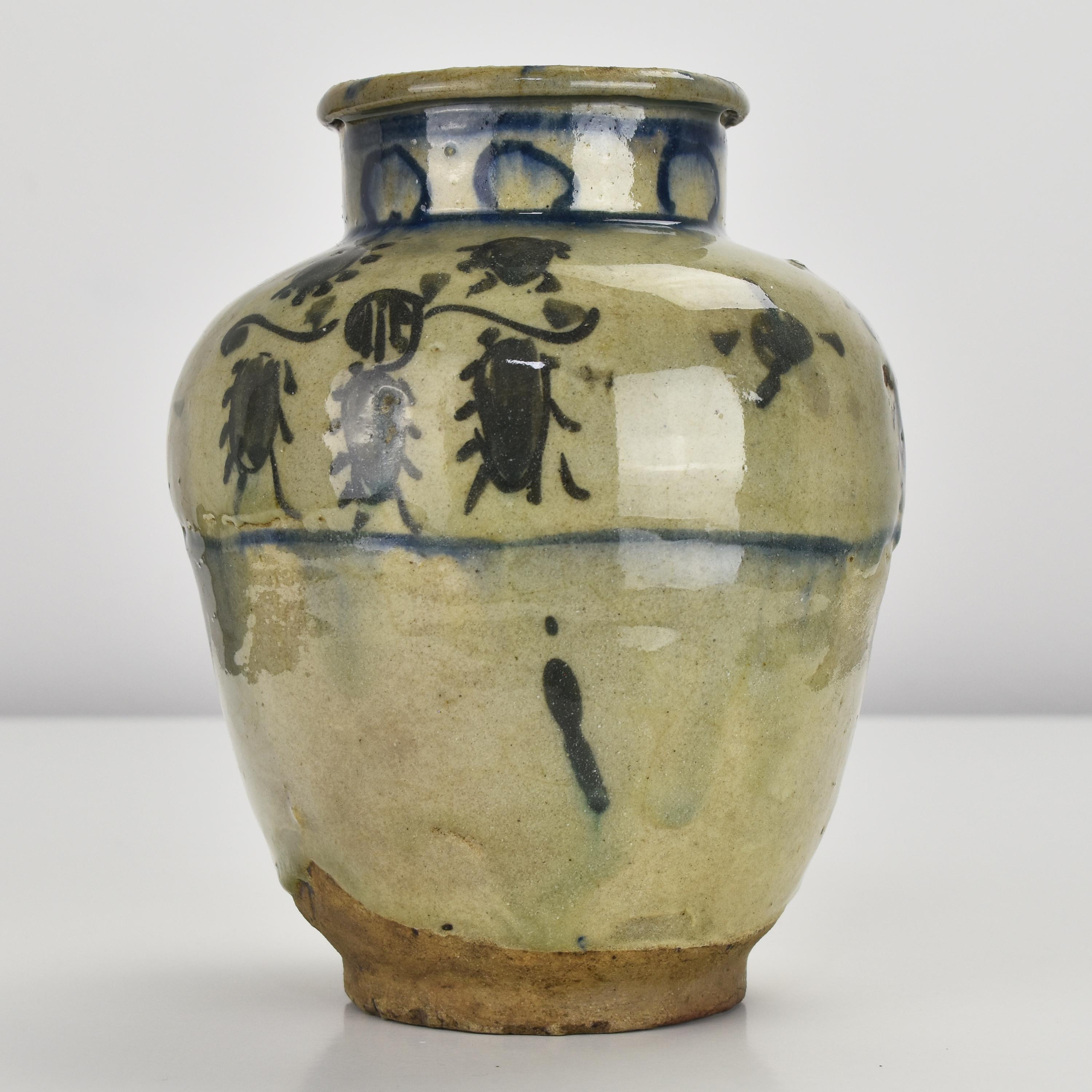 This antique ceramic jar or vase is believed to be from the 15th century and is of the Mamluk period. It is made of a sandy earthenware and features a thick glaze. The jar is decorated with polychrome handpainted floral elements in green to the body