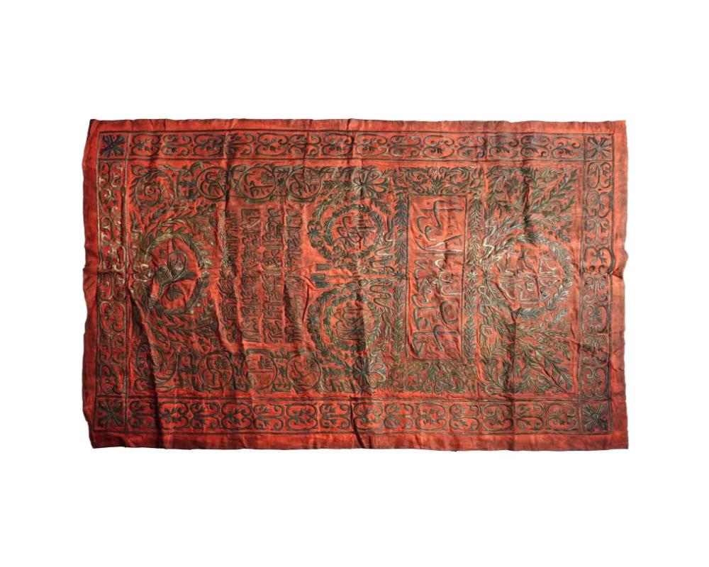 A large antique Islamic metal-thread embroidered red velvet panel of rectangular form. The central panel is adorned with calligraphy, surrounded by additional inscriptions in a decorative floral interlace. The border is adorned with undulating