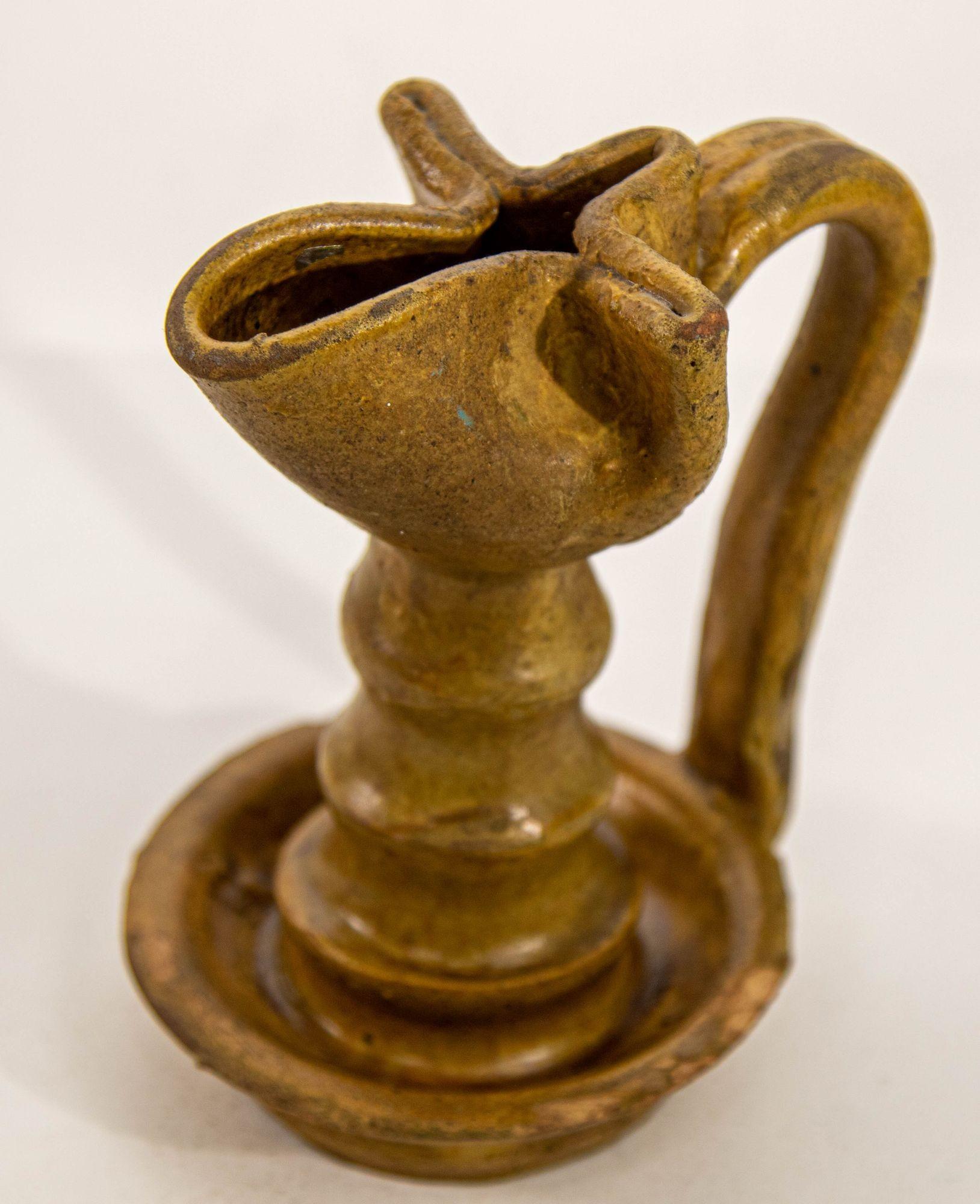 Antique Islamic Persian Nishapur style ceramic glazed oil lamp.
A stunning brown pottery oil lamp in the unique Nishapur style.
A pinched top bowl, with its narrow spout for a wick, sits atop a long, thin neck strap handle descends from top to